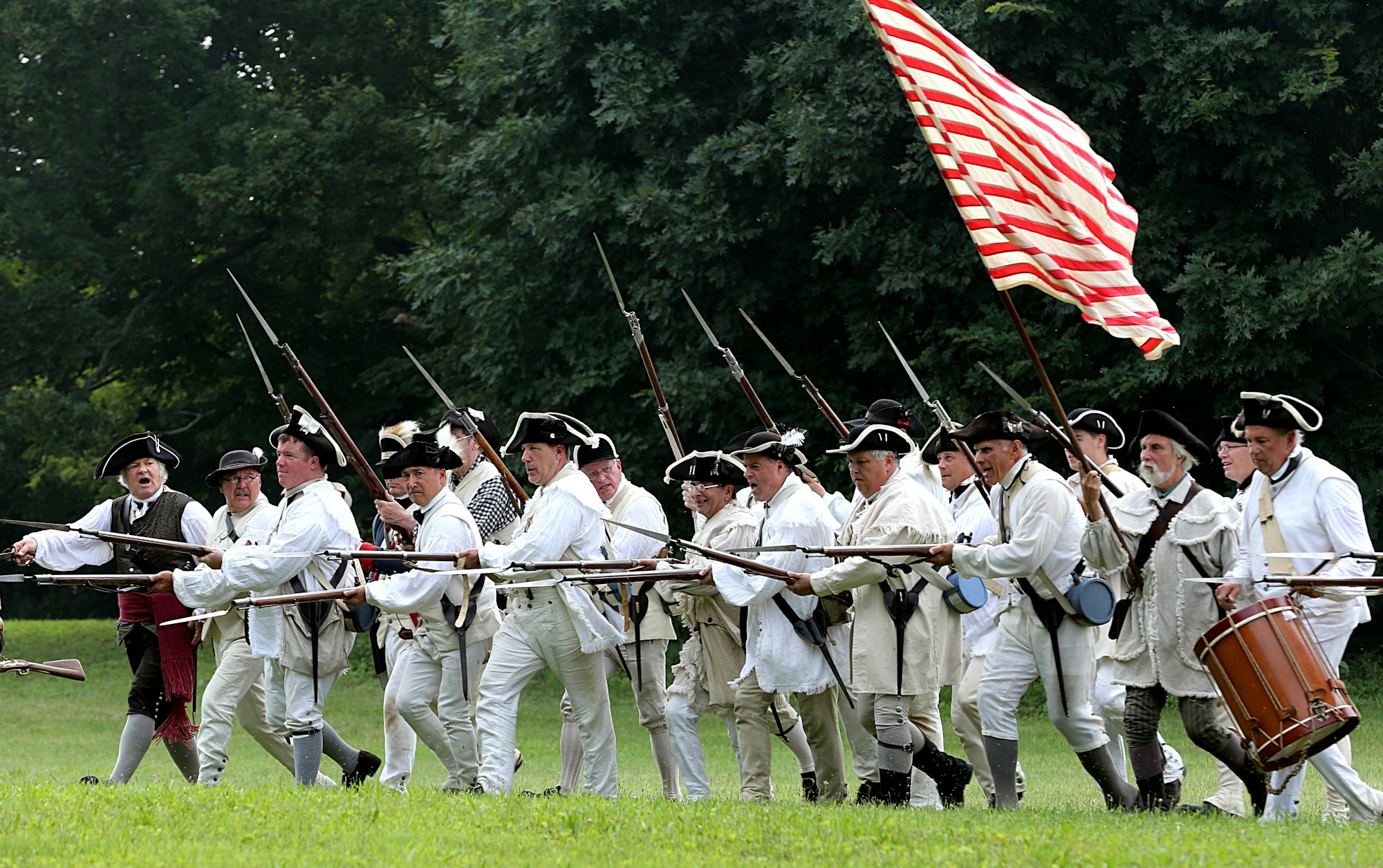 Reenactors shouldering muskets behind a colonial flag in Virginia.
