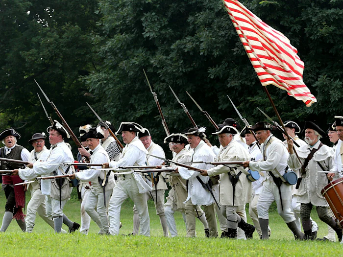 Reenactors shouldering muskets behind a colonial flag in Virginia.