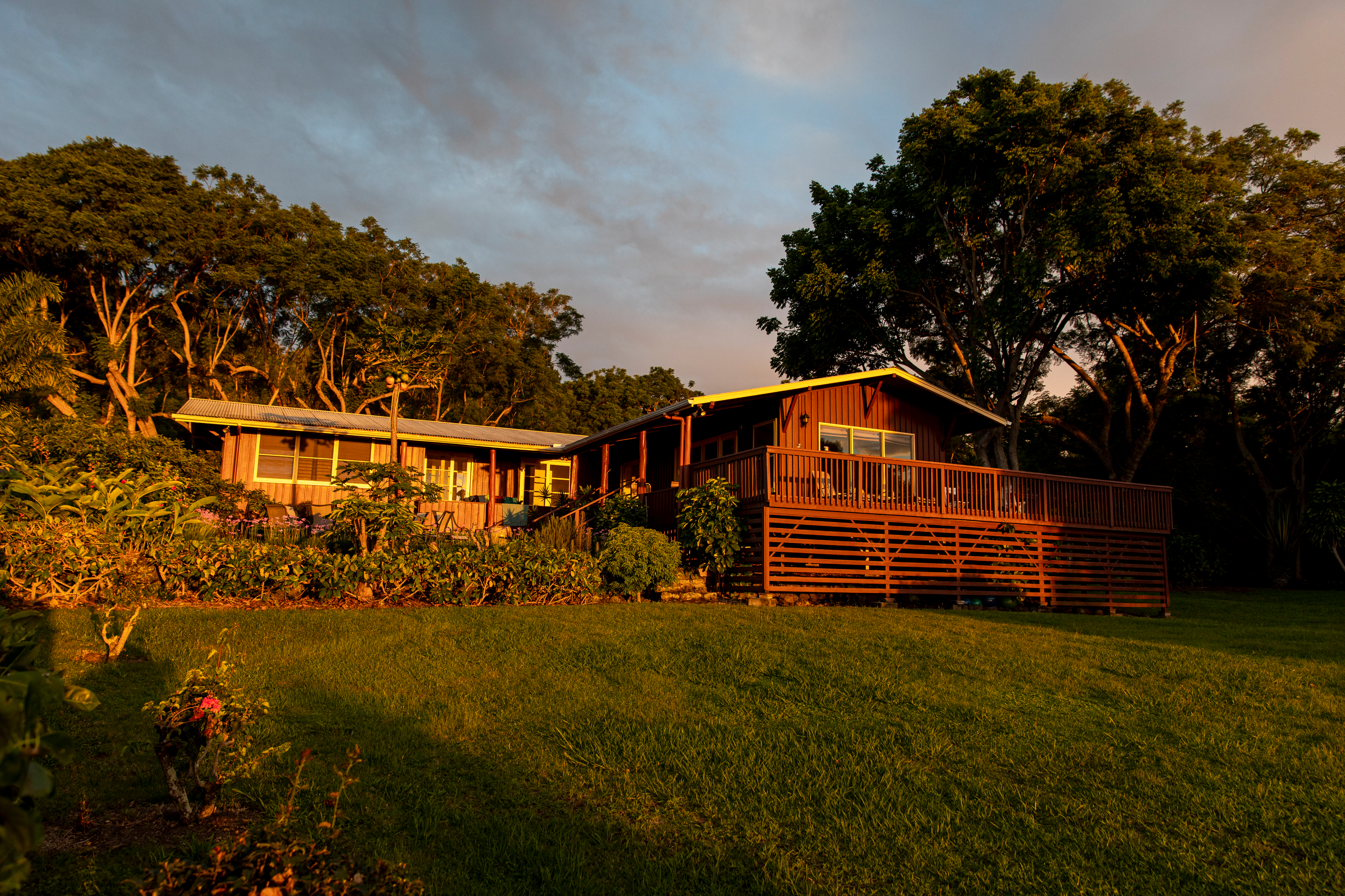 A wooden lodge with a deck sits among trees at sunset, framed by a grassy lawn