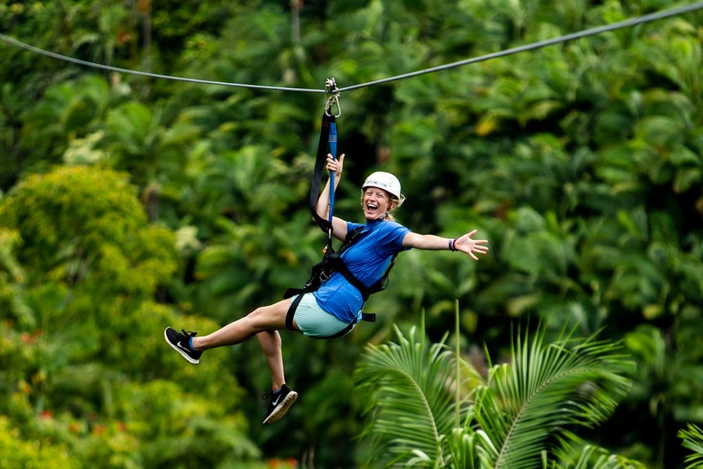 Teen tour participant ziplining over a forest in Hawaii, USA.