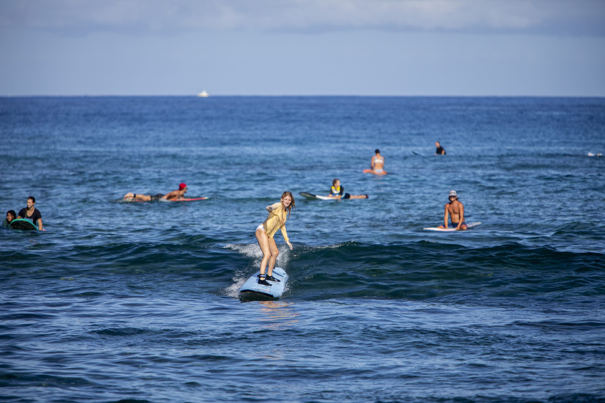 A surfer riding a wave in the ocean, with other surfers in the background.