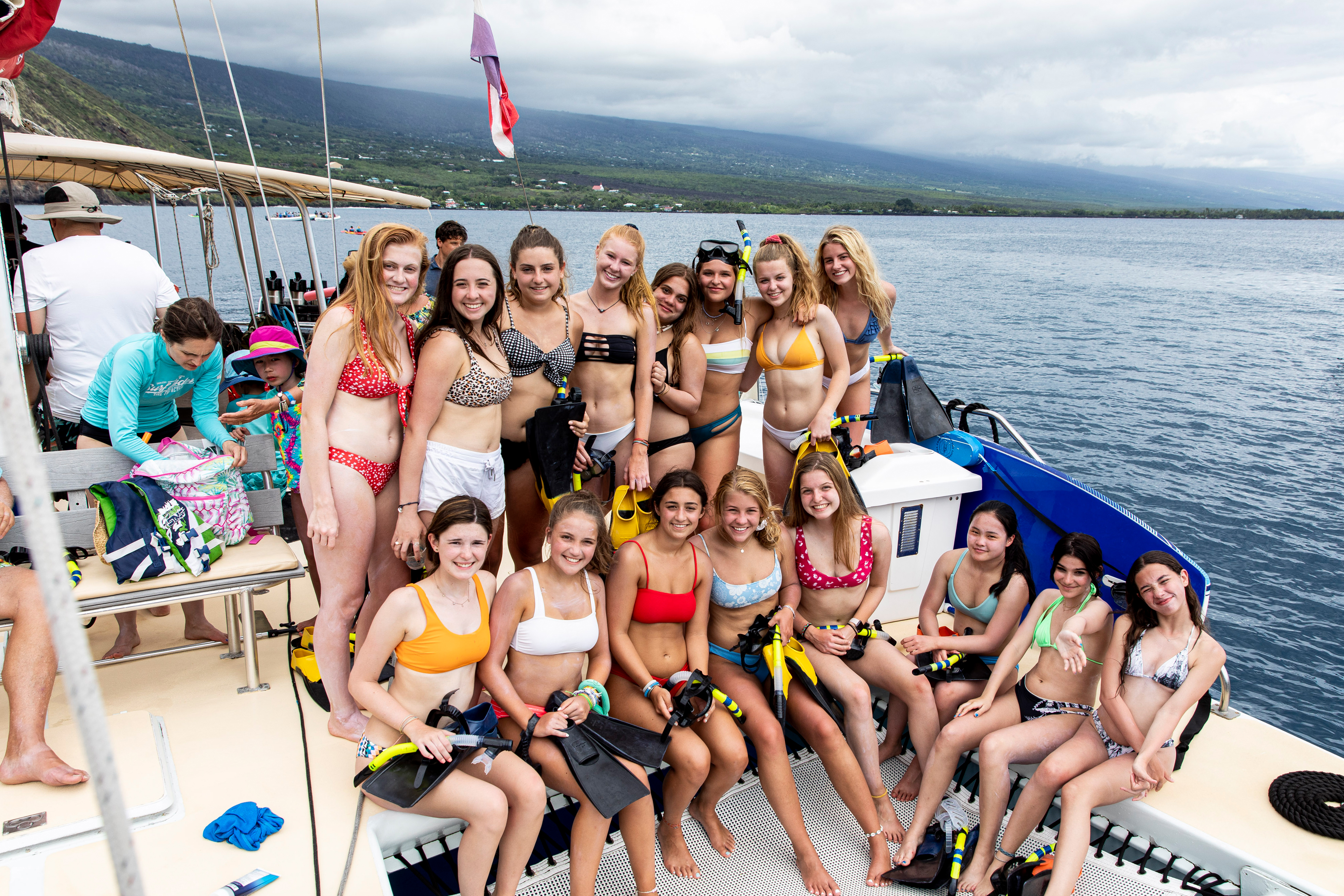 Students in snorkel gear pose together on a boat deck with mountains in the background