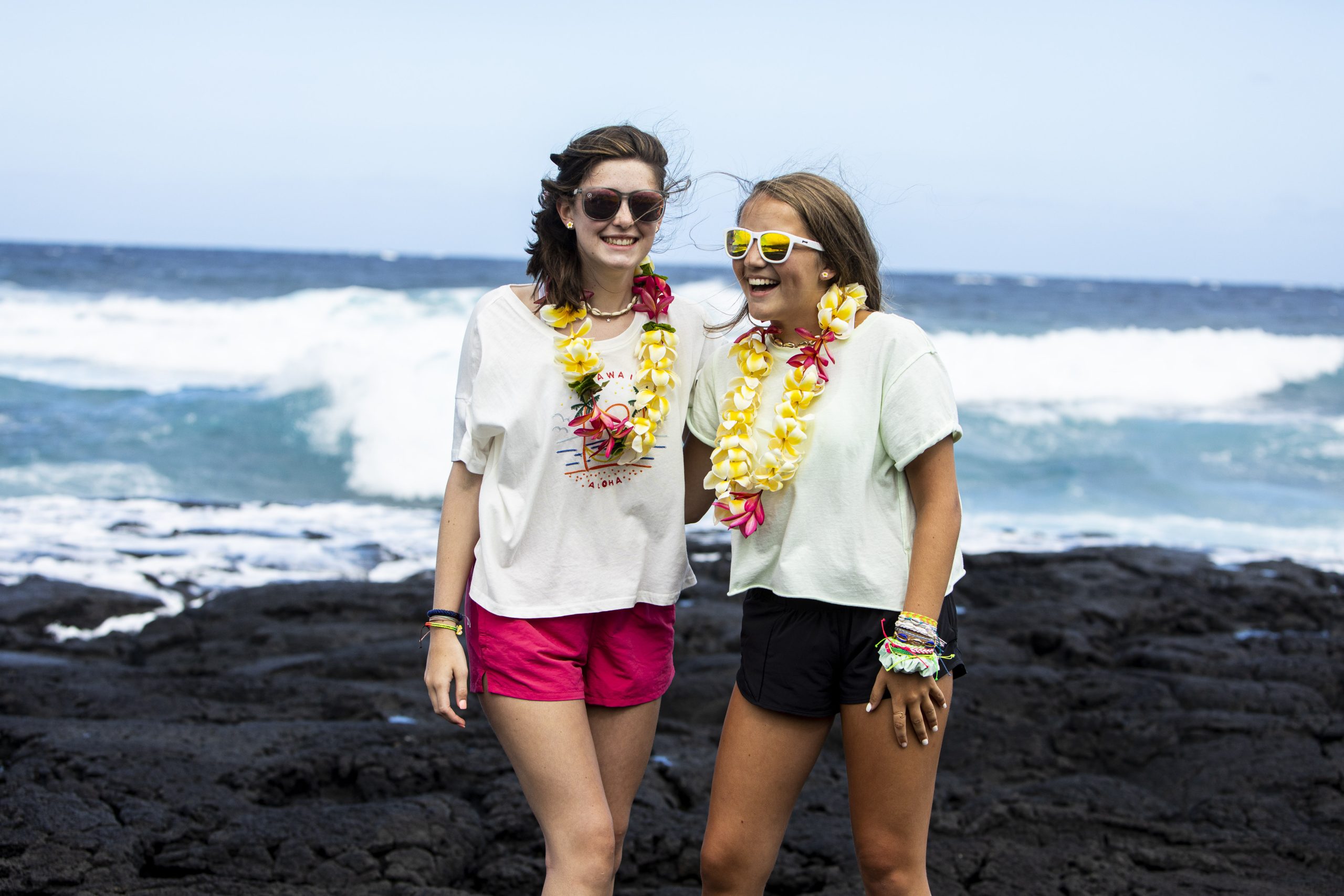 Two students smiling on a black-sand beach in Hawaii during a Rustic Pathways volunteer abroad program, representing positive student reviews and travel experiences abroad.
