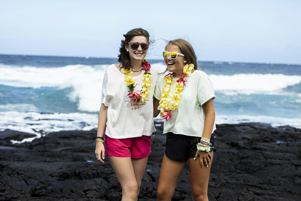 Two students smiling on a black-sand beach in Hawaii during a Rustic Pathways volunteer abroad program, representing positive student reviews and travel experiences abroad.