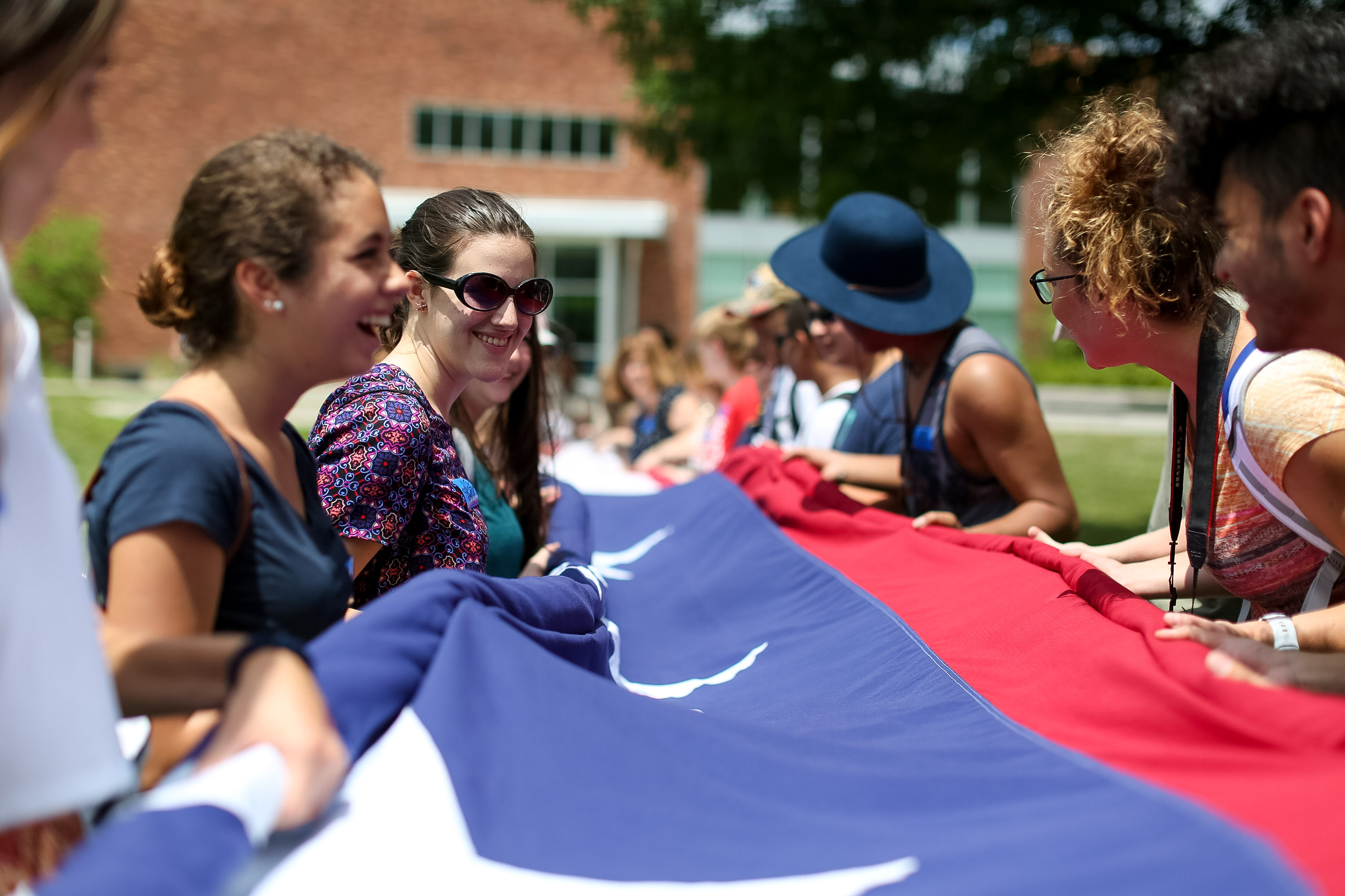 Students smile while folding a large American flag outdoors