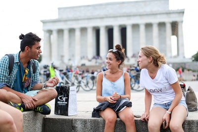 A group of student travelers share ideas while sitting in front of a columned building on a teen tour in the USA.