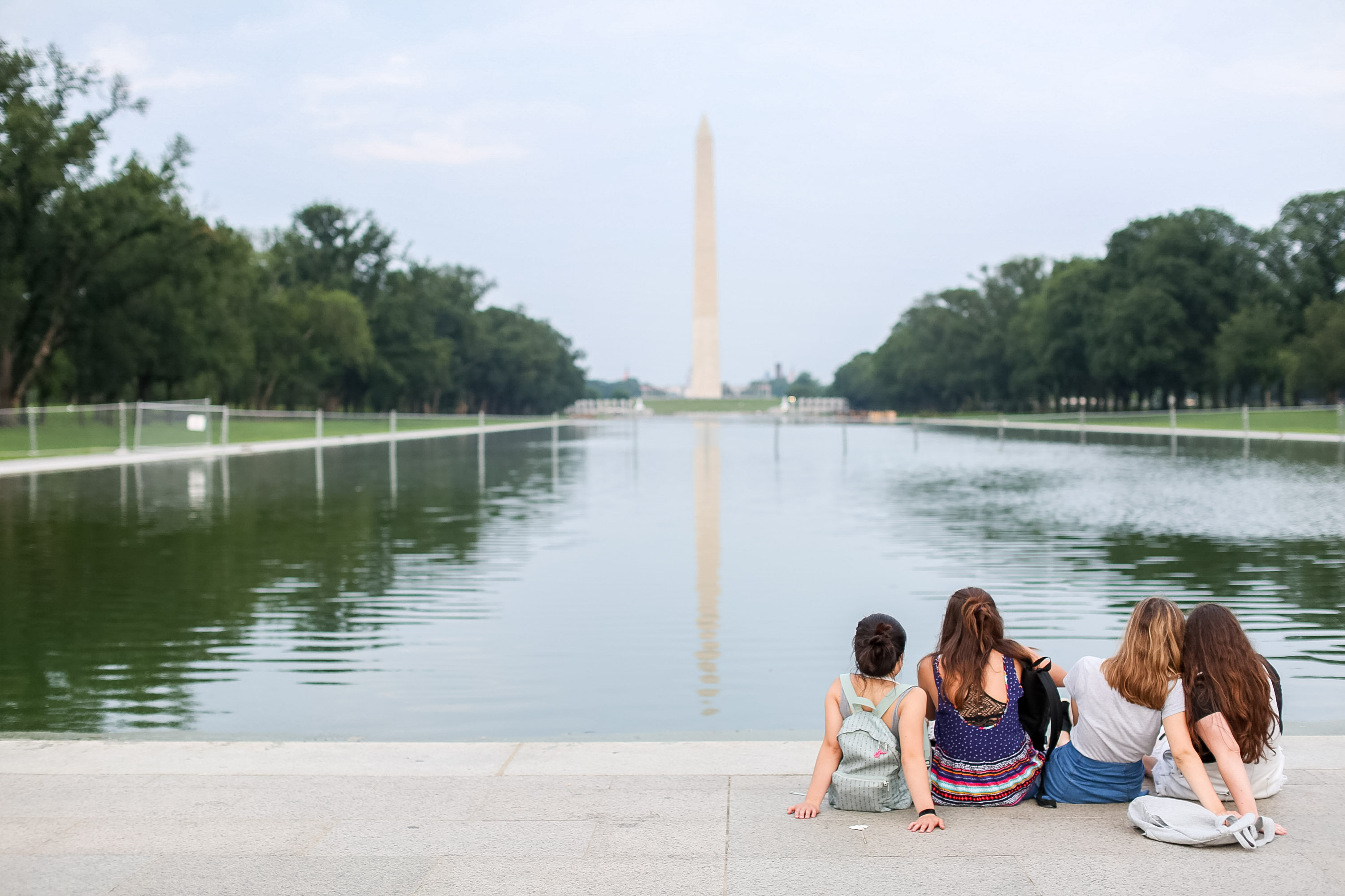 Students sit at the edge of the Reflecting Pool facing the Washington Monument.
