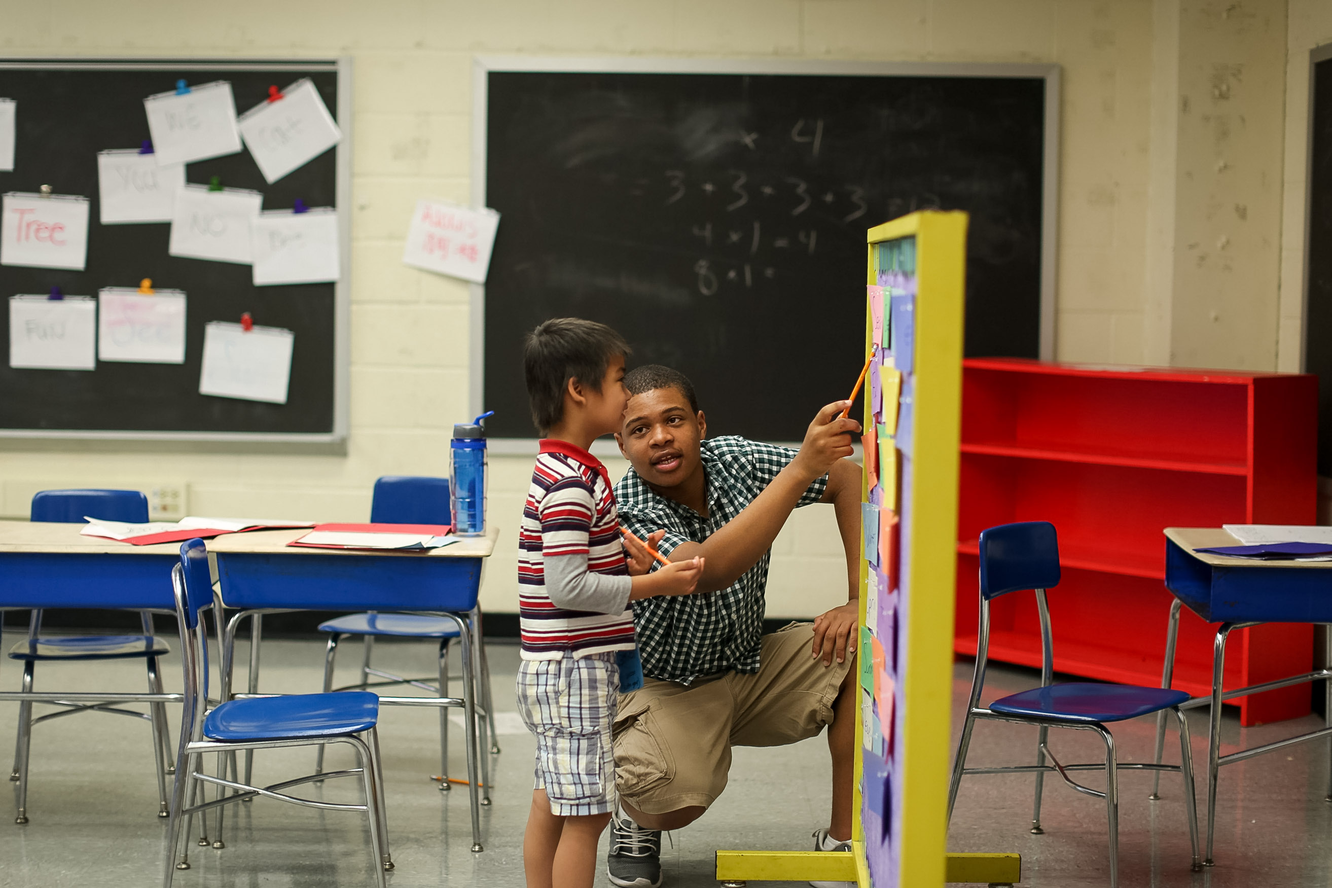 On this school trip a volunteer helps a young student point to a colorful display board in a classroom