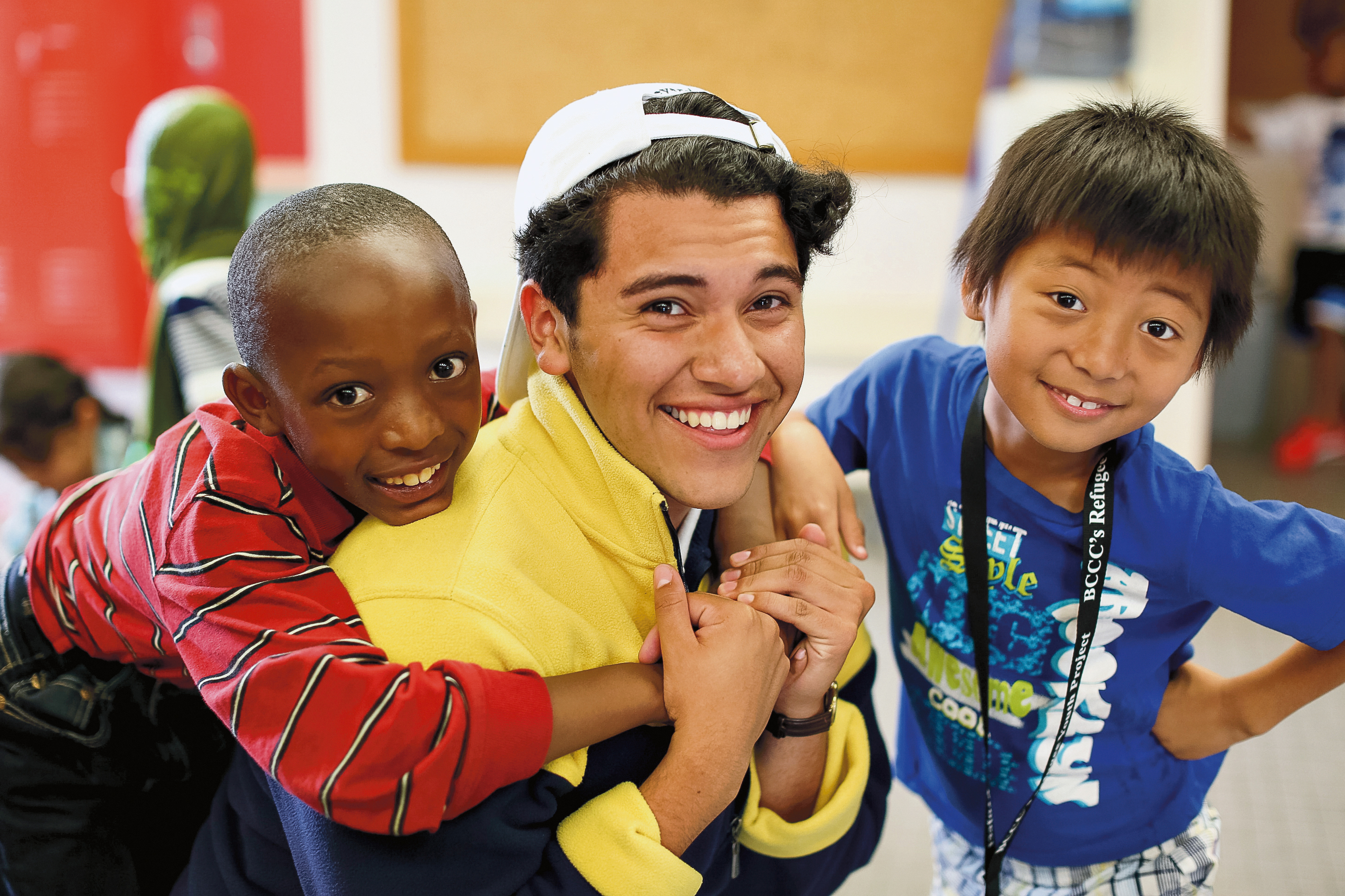 A student smiles while giving a child a piggyback ride indoors, with another child posing alongside