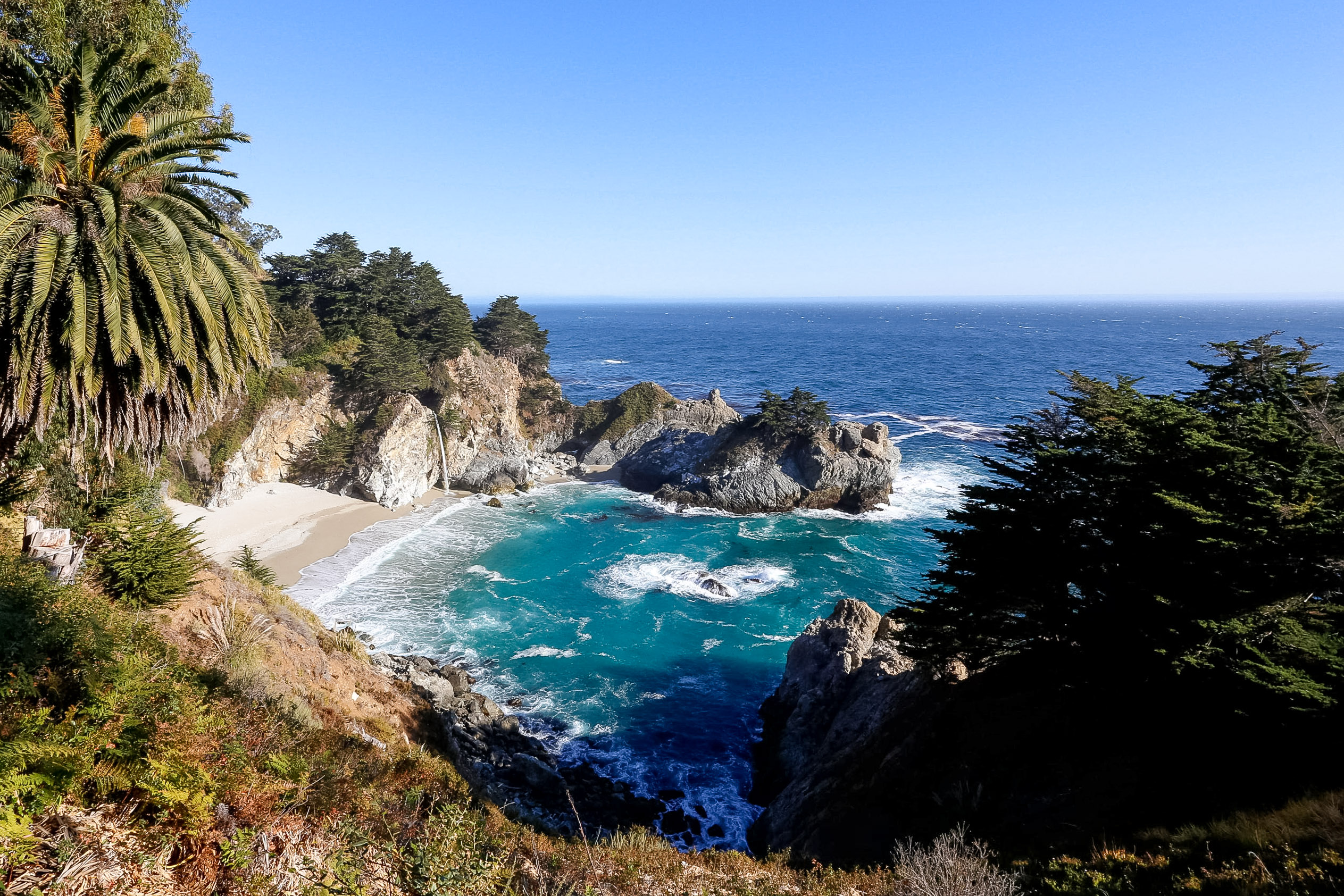 A rocky cove along the Big Sur coastline with turquoise water and palm trees