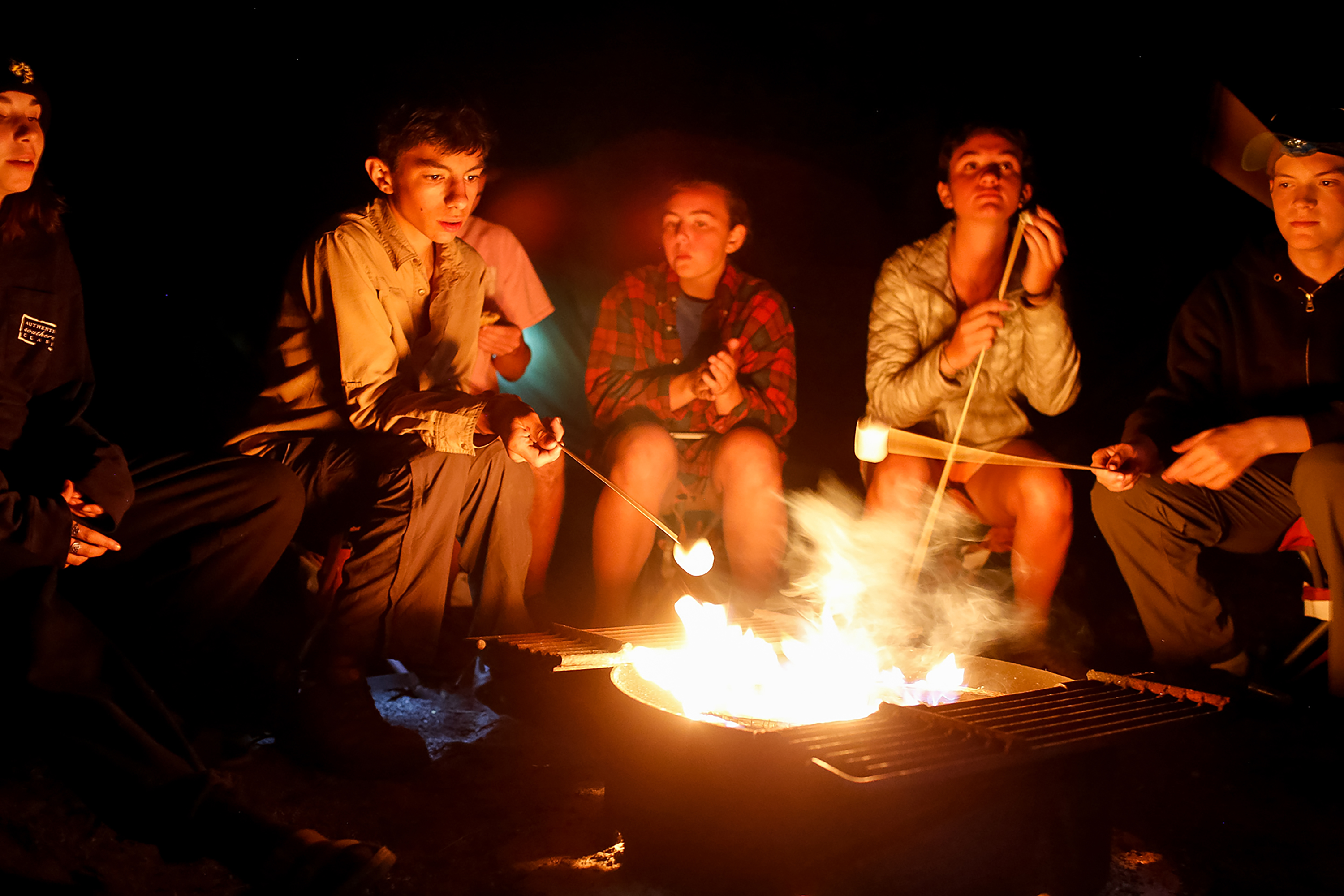 Students sit together around a campfire while making s'mores.