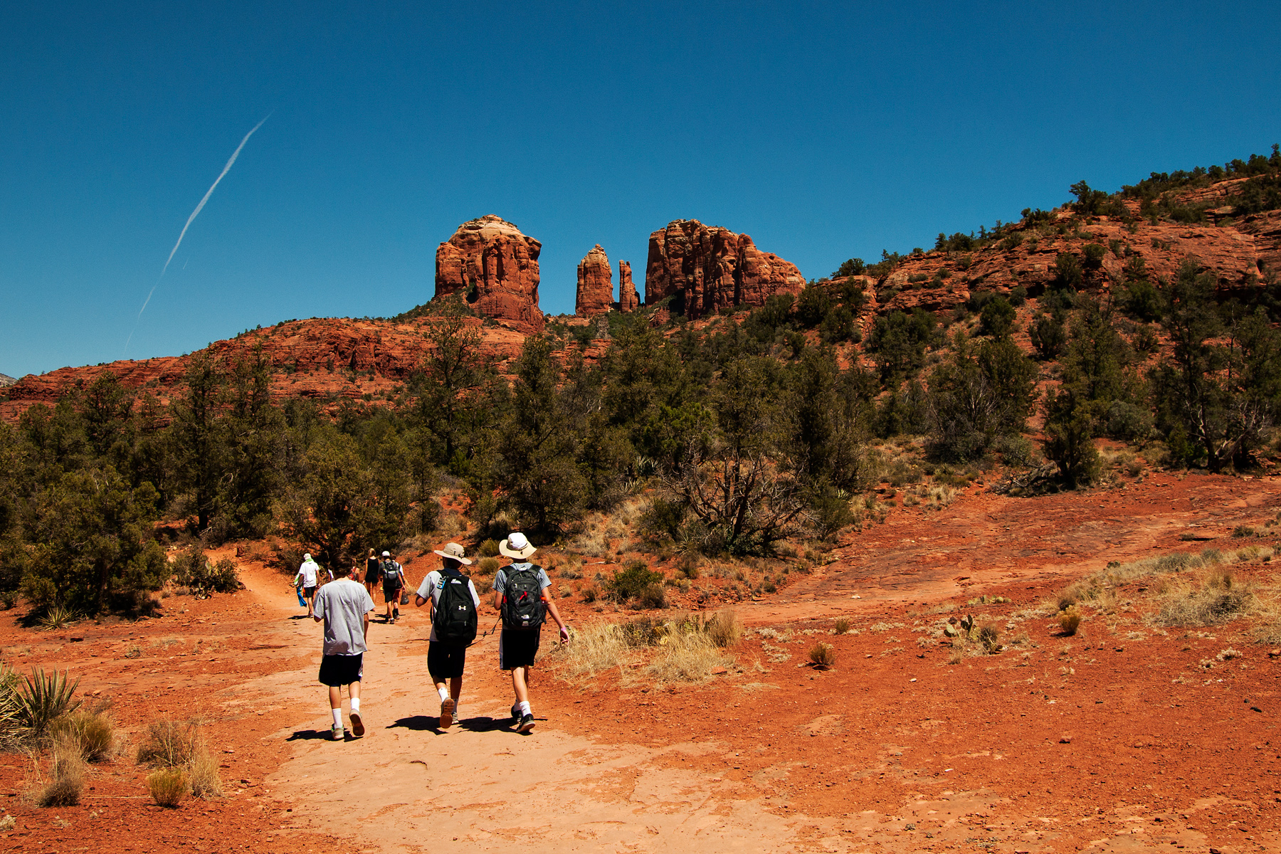 Teen travelers hike a red dirt trail toward Sedona's red rock formations