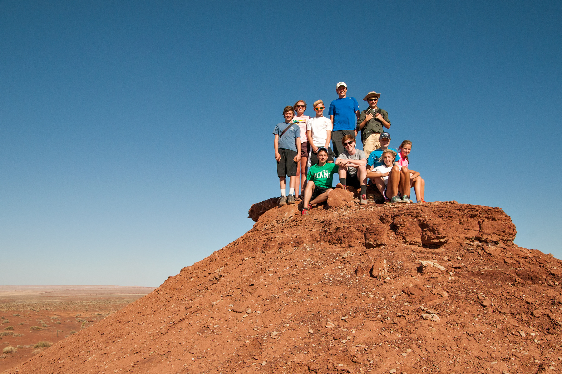 Students pose atop a red rock formation under a clear desert sky