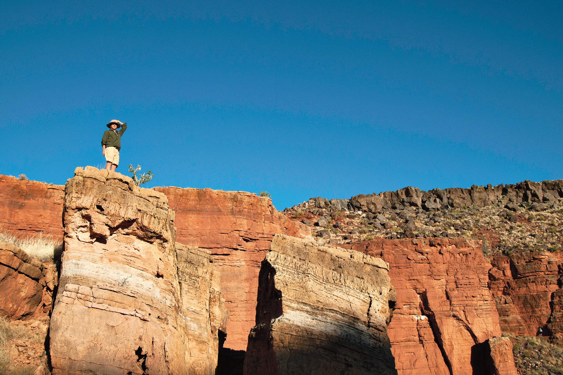 On this school trip a student stands atop a red rock formation against a clear blue sky