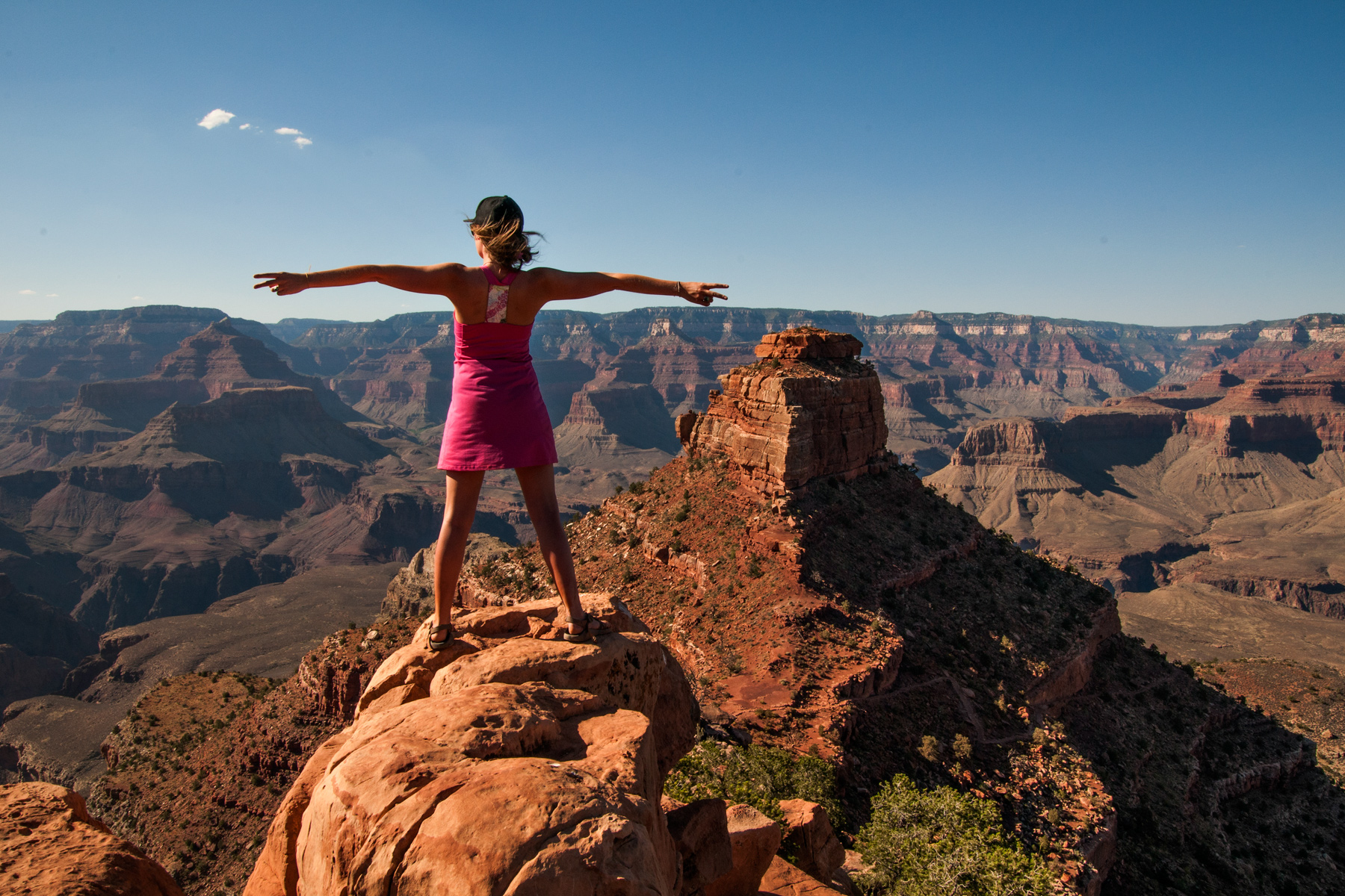A student stands on a rock outcrop with arms outstretched overlooking the Grand Canyon in the United States