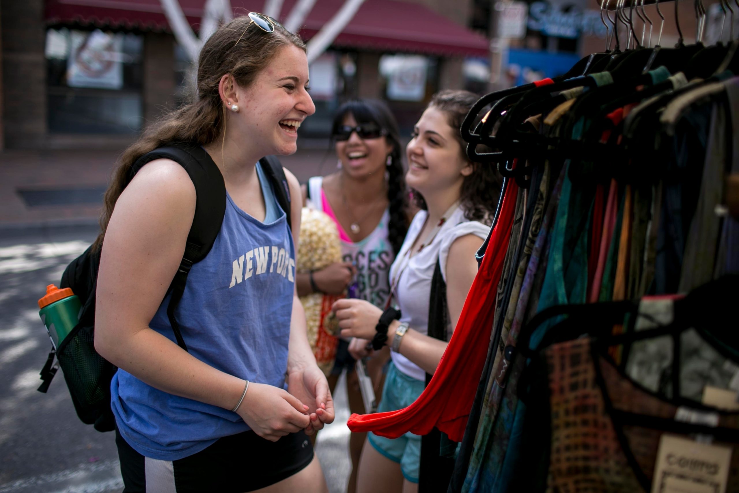 Students laugh while browsing colorful scarves at an outdoor market stall