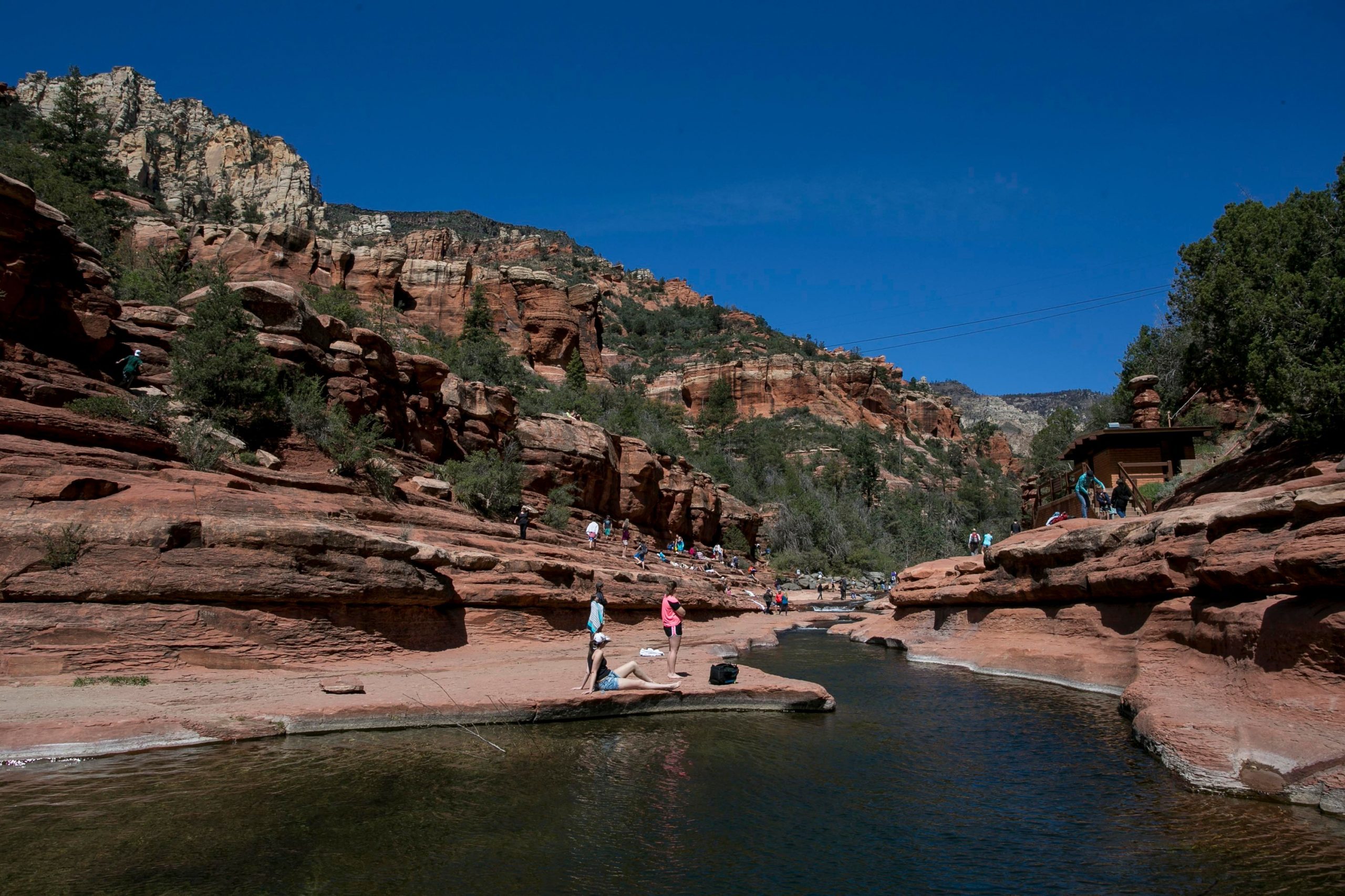 A red-rock canyon with a calm stream where students relax along the water's edge
