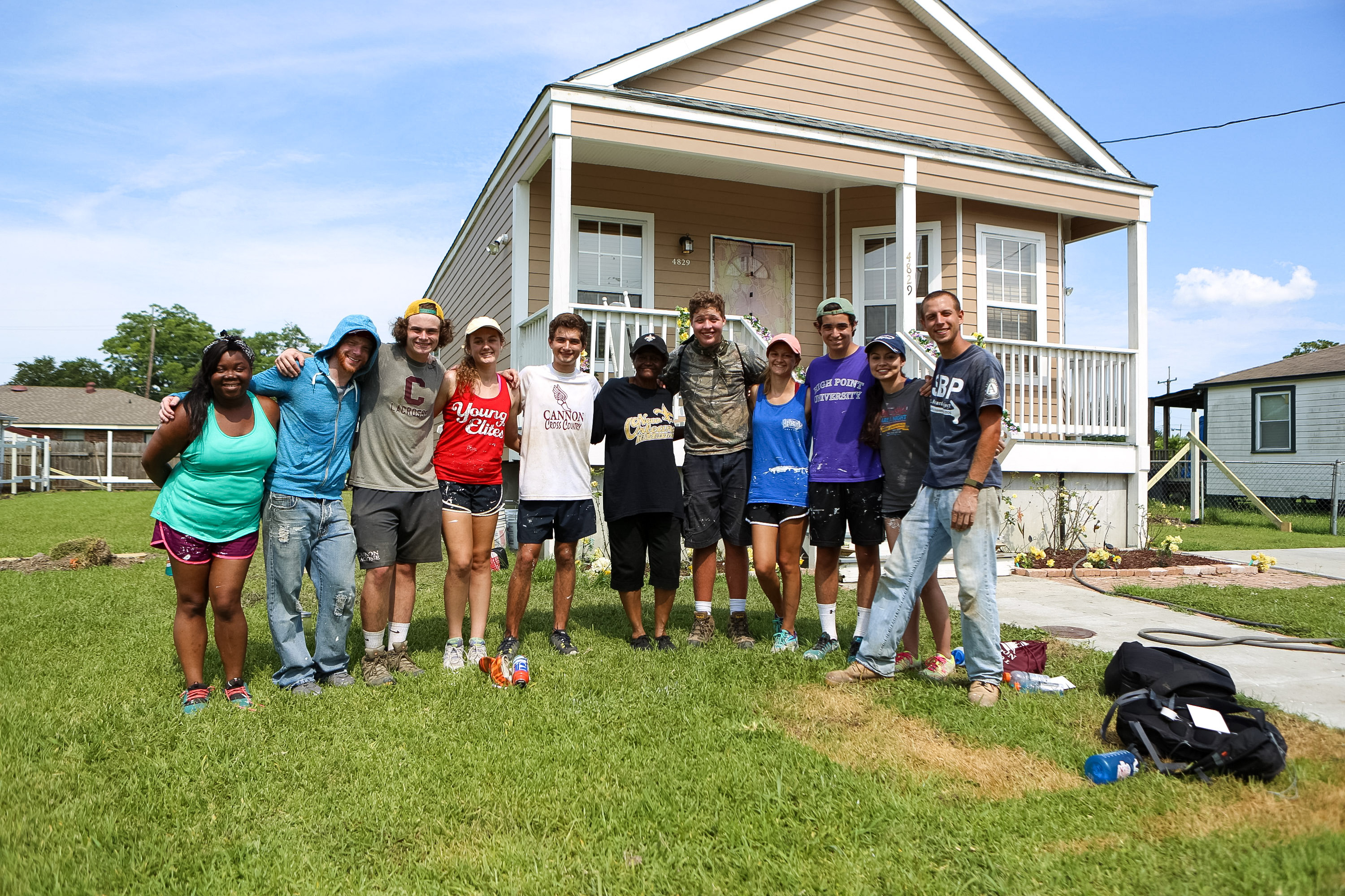 Students pose together on a lawn in front of a rebuilt house
