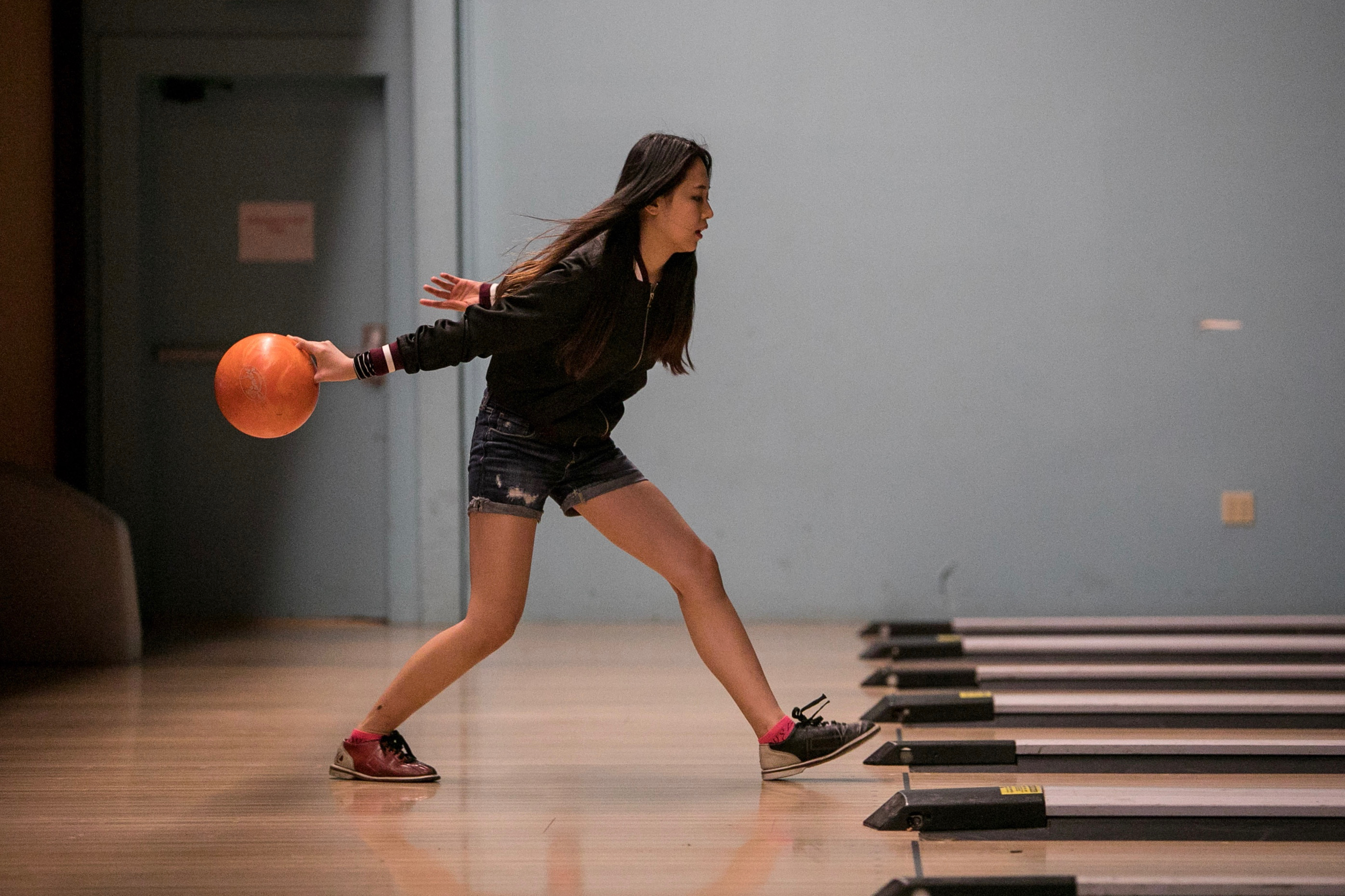 Student bowling about to throw an orange bowling ball.