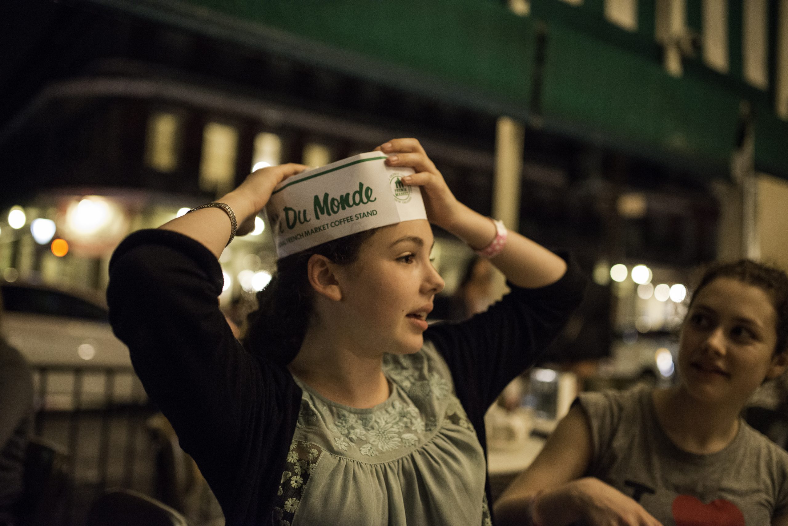 A woman playfully adjusts a paper hat on her head while sitting at a lively seafood restaurant, surrounded by others enjoying their meals. fun facts about new orleans