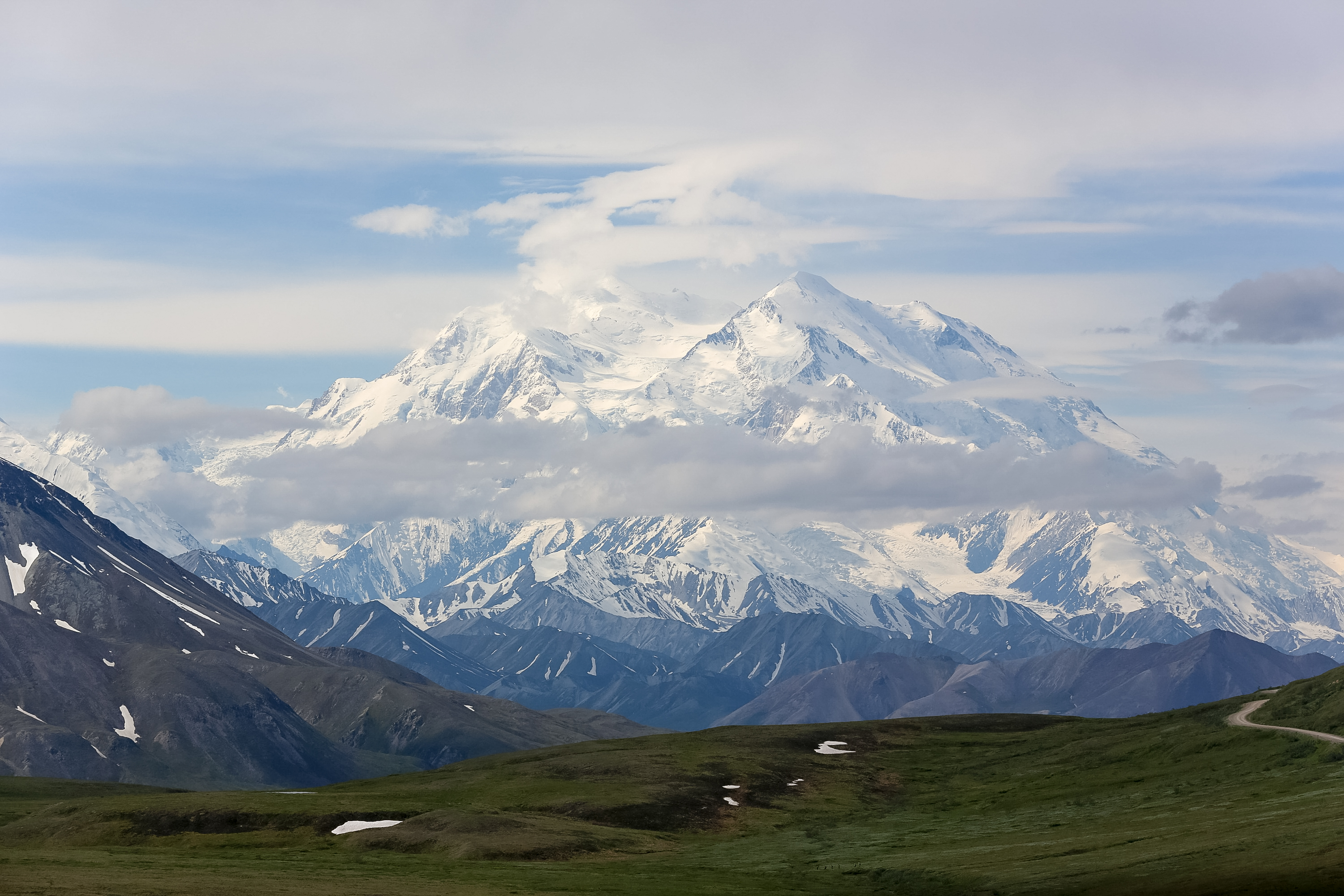 A school trip pauses along a winding gravel road as a snow-capped mountain peak rises above green tundra