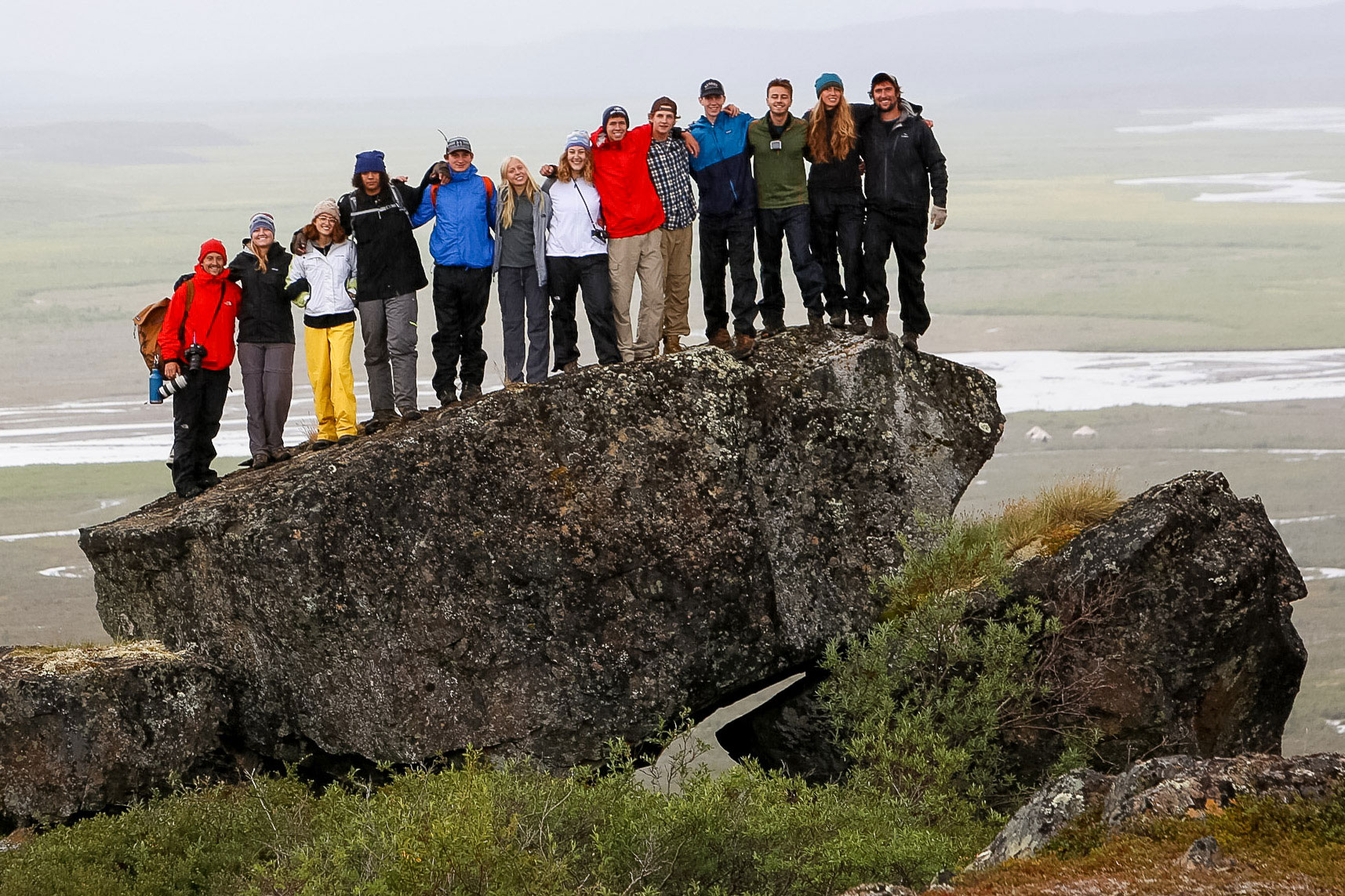 Students pose atop a large rock overlooking a misty Alaskan valley