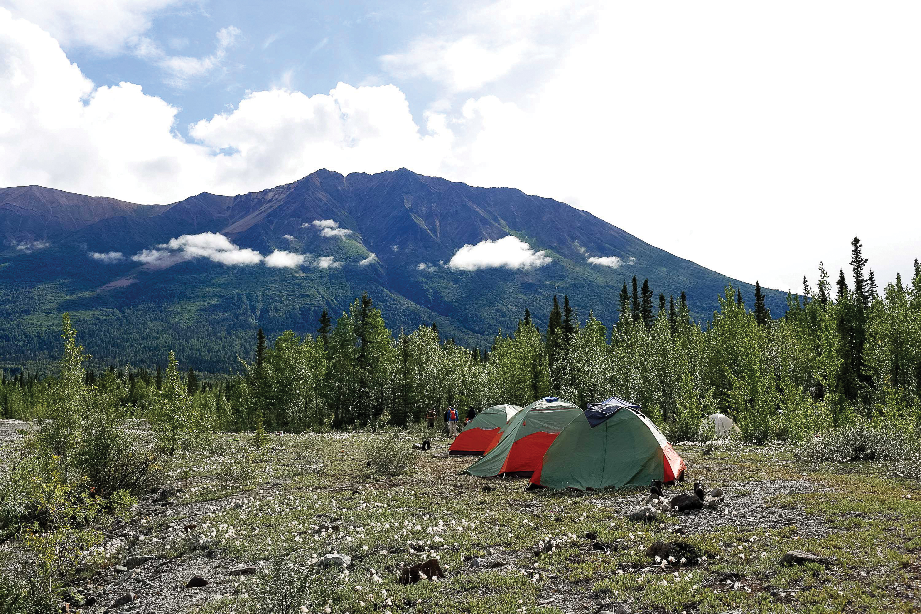 Tents pitched in a wilderness clearing beneath a mountain range