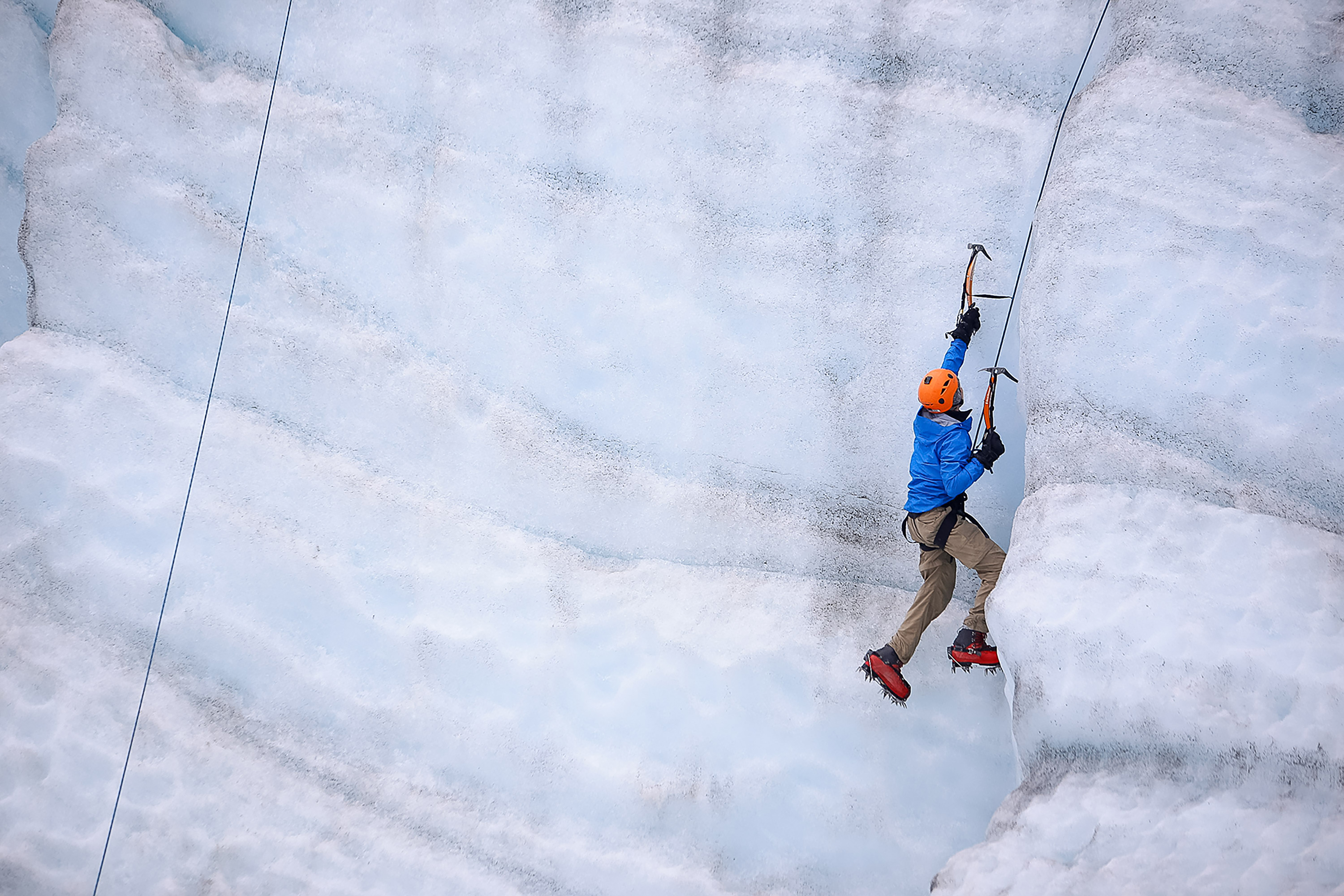 A student ice climbs a glacier wall using ice axes and crampons
