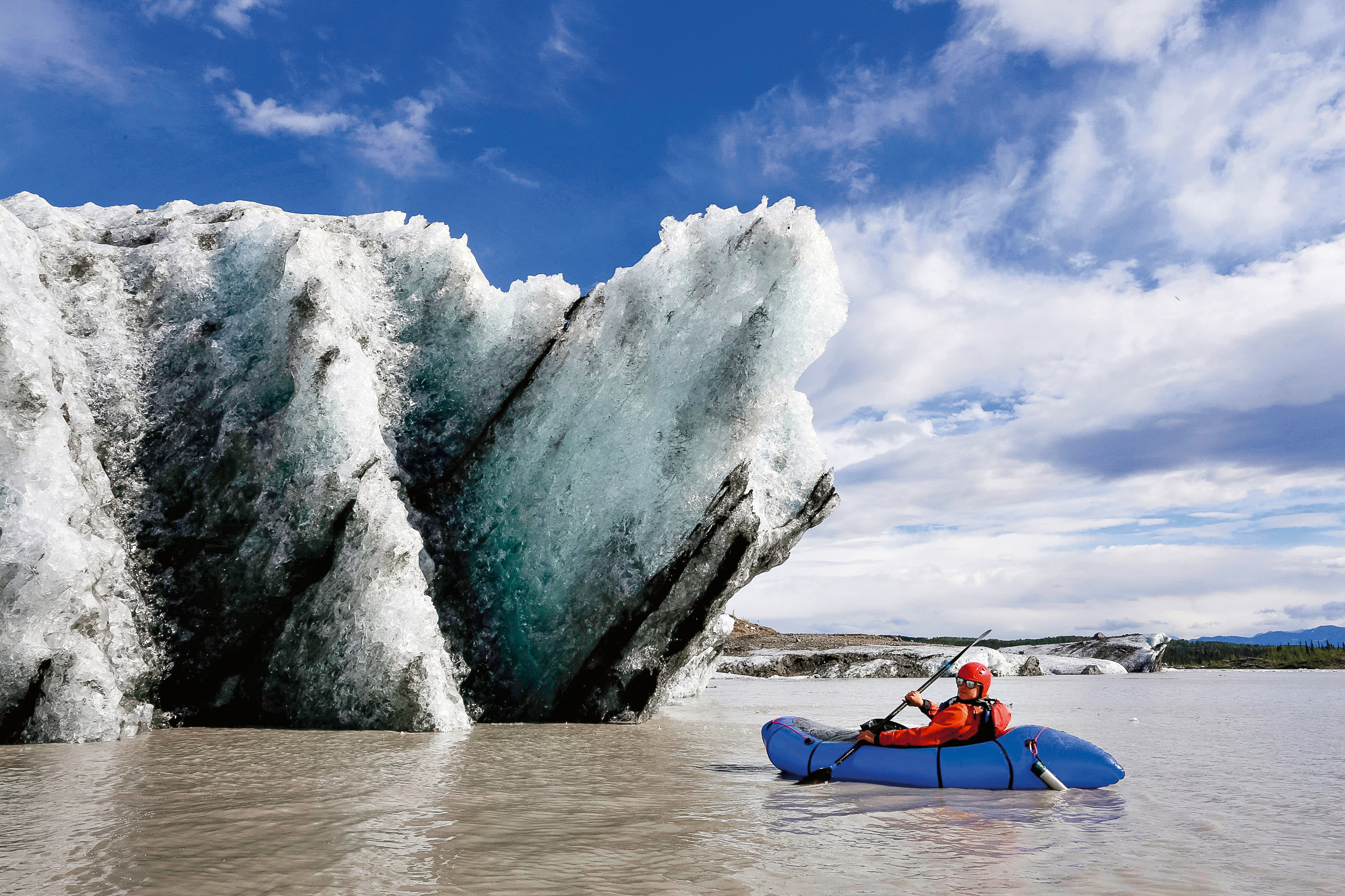 A student paddles a packraft near a jagged blue-ice glacier wall