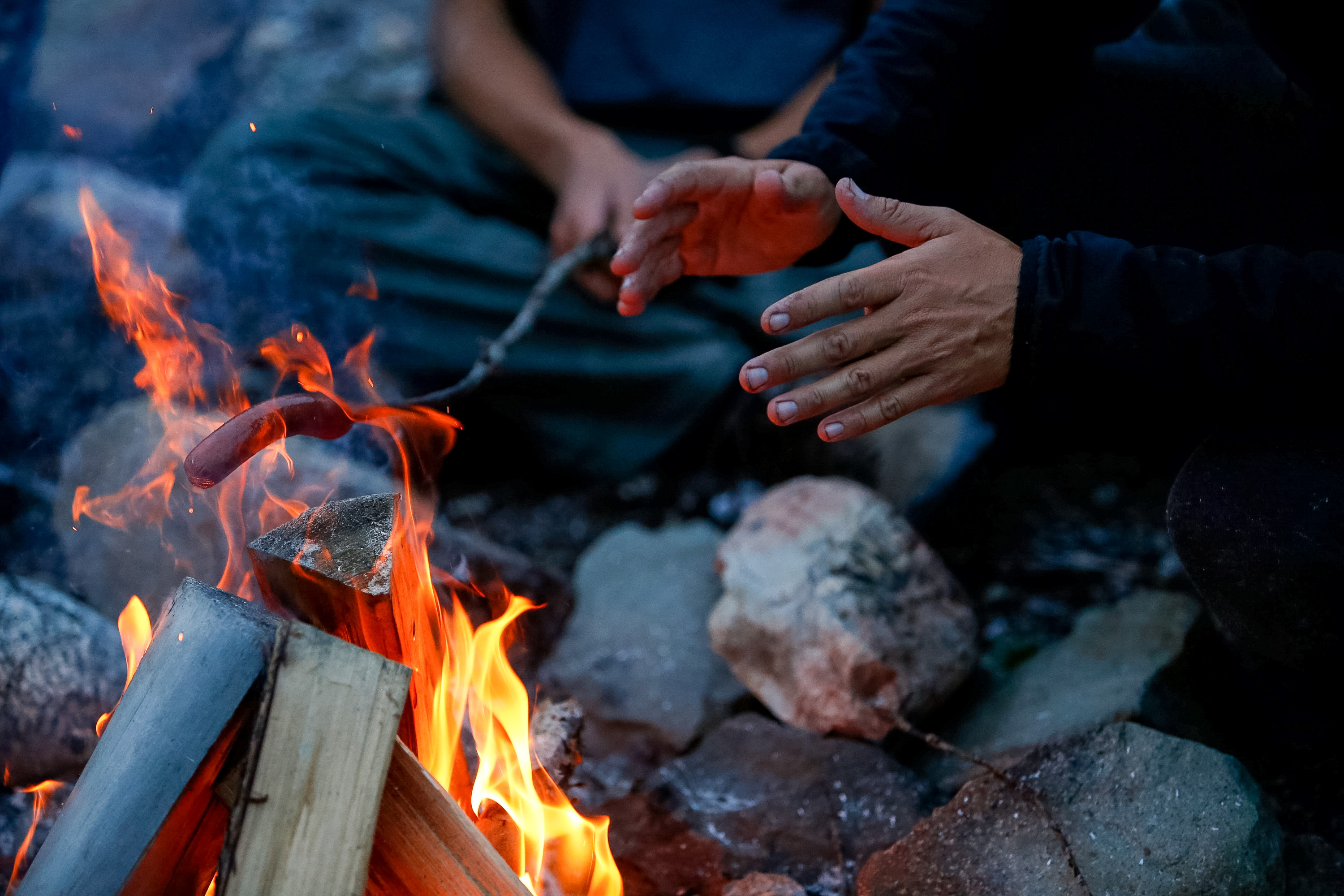 Students warm their hands by a campfire cooking over the flames