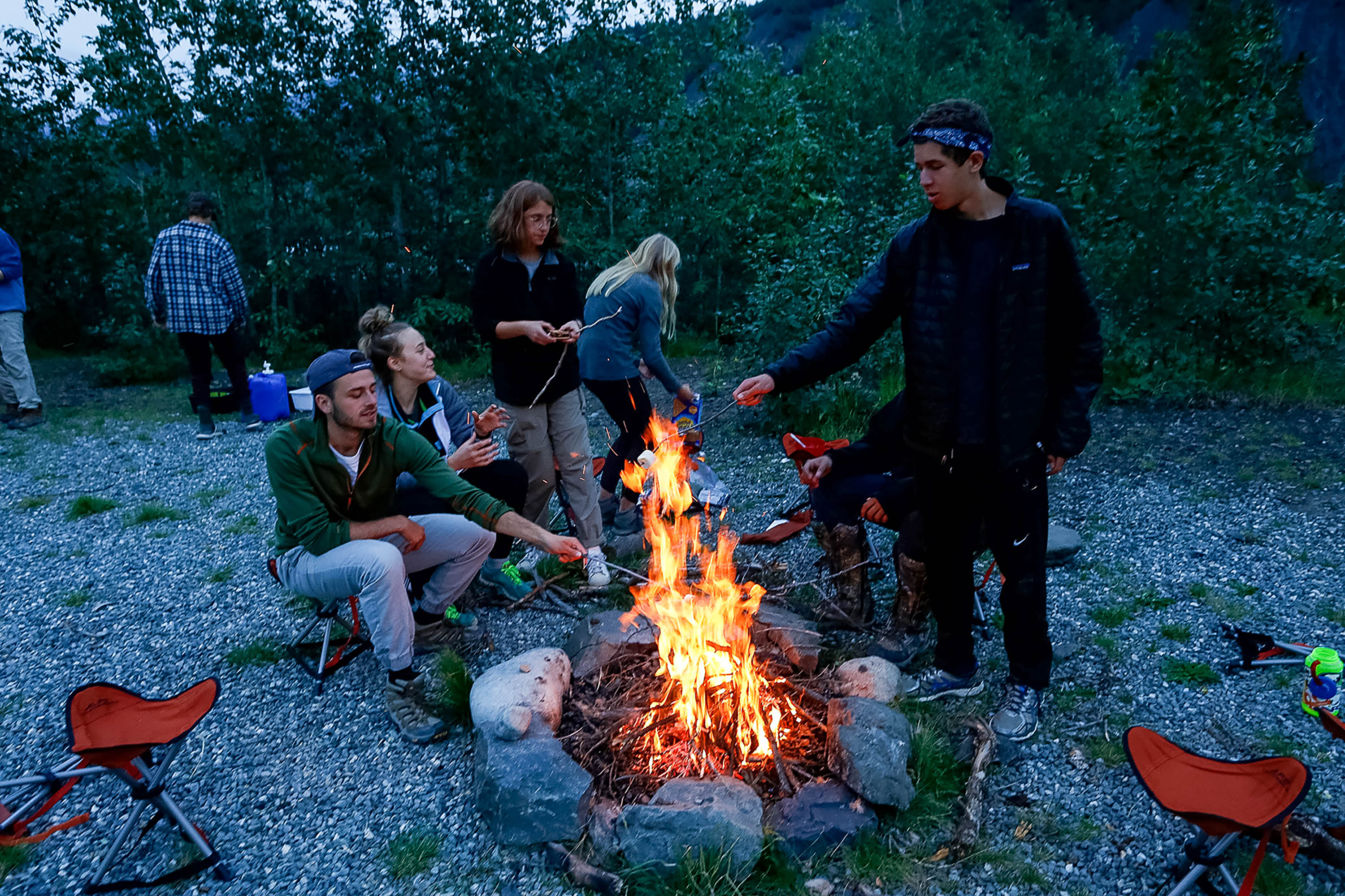 Student travelers gather around a campfire in the woods at dusk