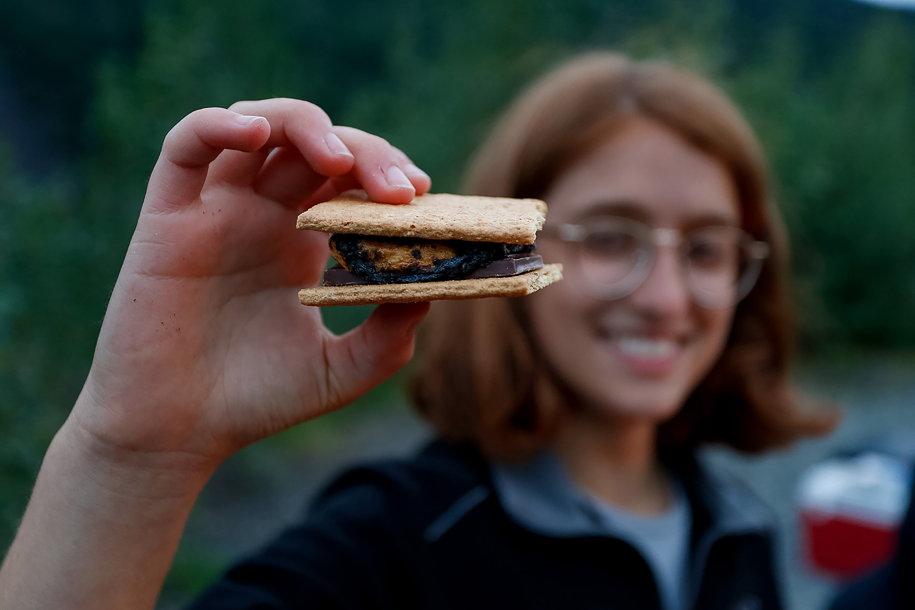 A student holds up a s'more, smiling in the evening light