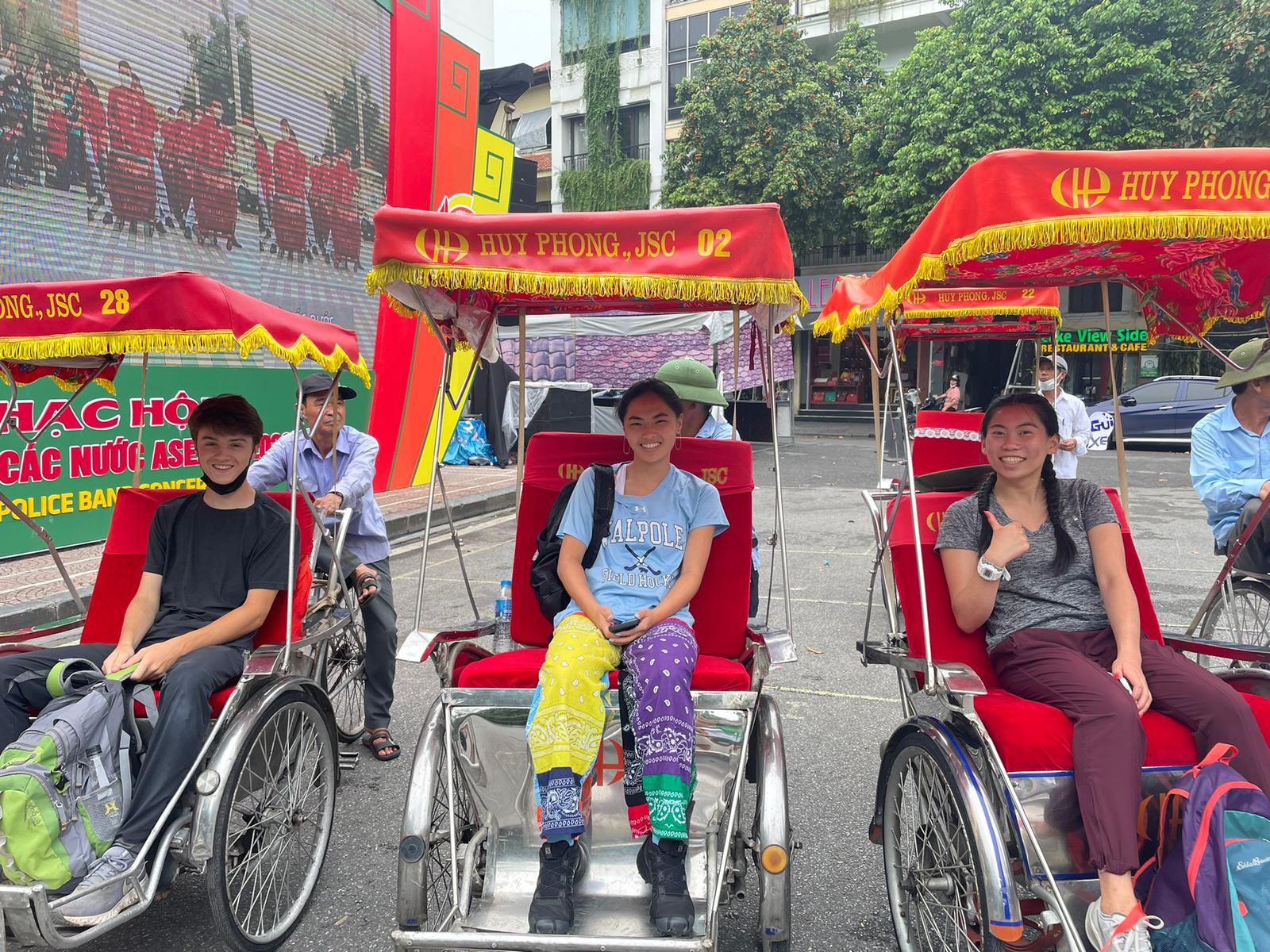 Students ride in decorated cyclos on a Hanoi street