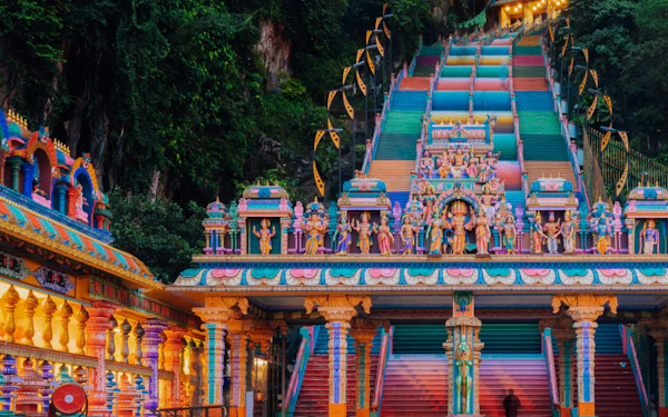 Colorful rainbow-painted stairs lead up to the ornate entrance of Batu Caves temple at dusk.