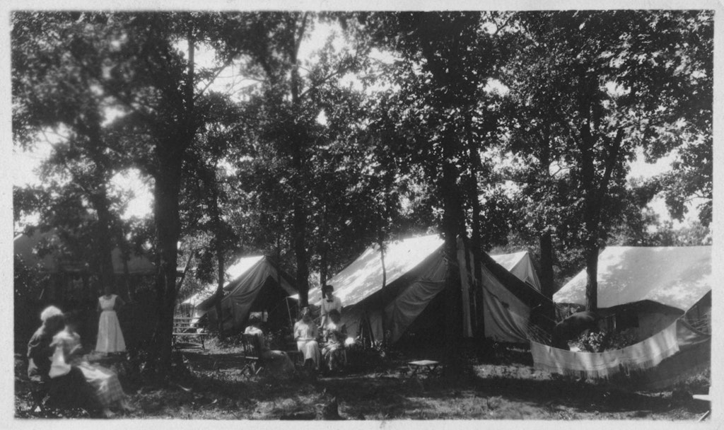A vintage photo of a summer camp at Lake Calhoun, featuring tents, campers, and the surrounding natural landscape.