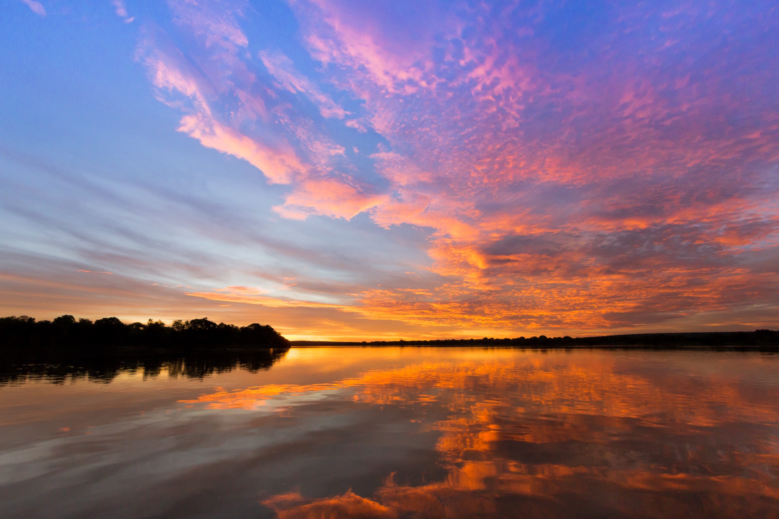 A vivid sunset over the Zambezi River at Matetsi in Zimbabwe, with pink and orange clouds mirrored in still water