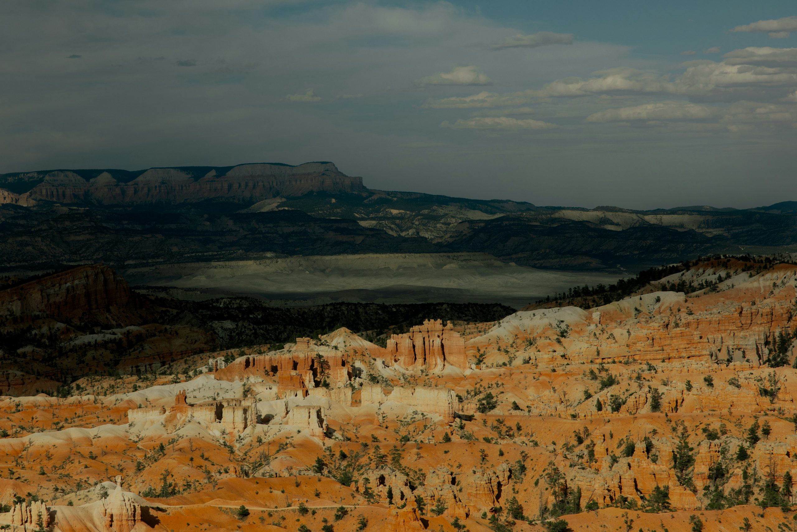 Orange hoodoos below a distant plateau under a darkening sky at Bryce Canyon.