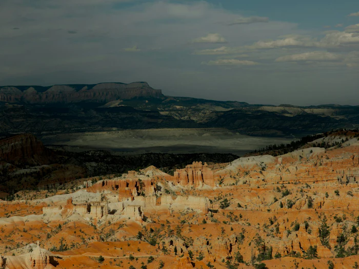 Orange hoodoos below a distant plateau under a darkening sky at Bryce Canyon.