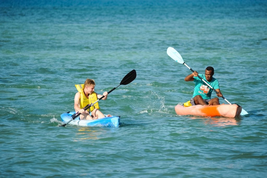 a student and a canoeing instructor rowing side-by-side on a calm ocean.