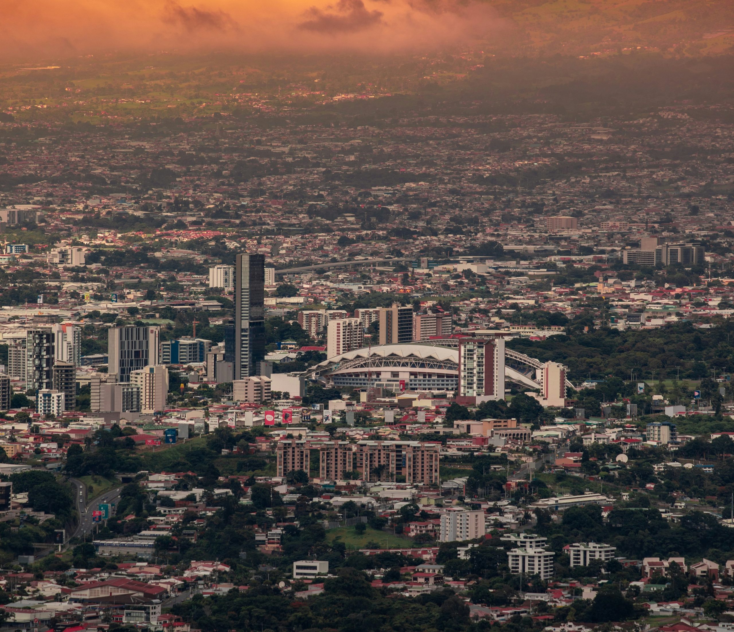 Rooftops of San Jose, Costa Rica, spread toward green hills under a bright sky.