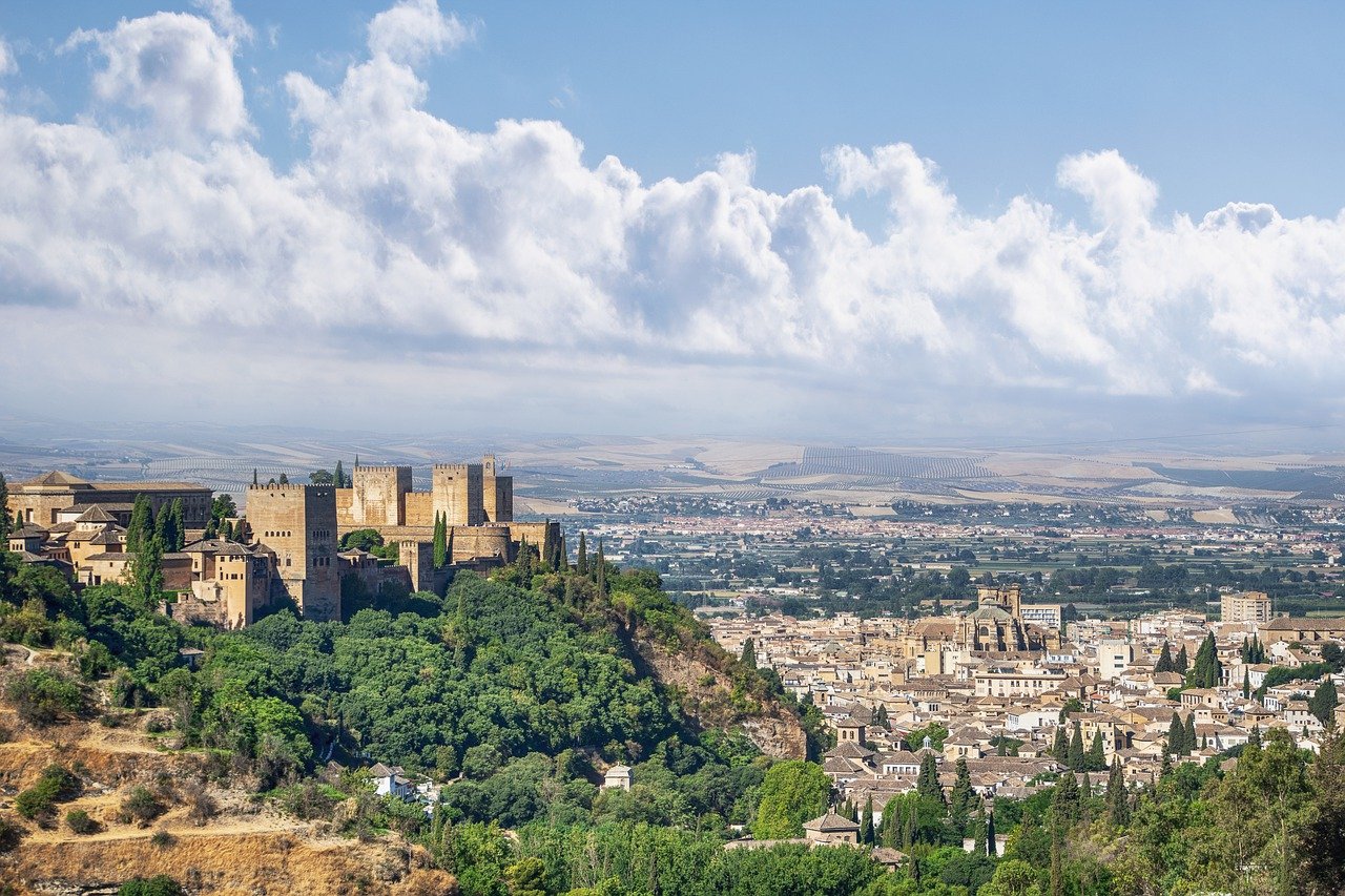 The Alhambra's fortress walls overlook Granada's rooftops beneath a cloud-filled sky