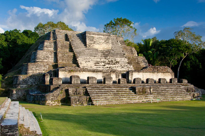 The main stepped stone temple at Altun Ha rises above a mown lawn under a blue sky in Belize