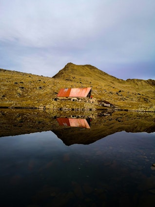 Mountain cabin reflecting in a calm lake, set against a rugged landscape in Bulgaria.