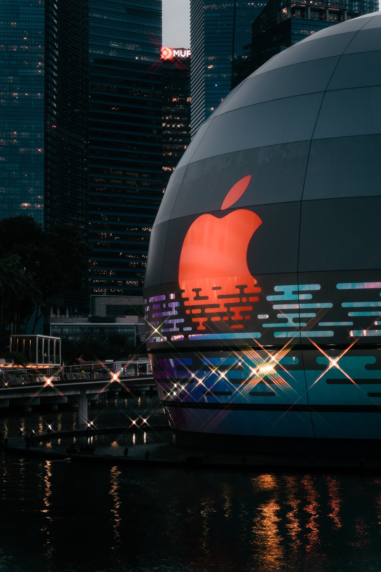 Illuminated glowing Apple logo on a spherical building against a city skyline at dusk