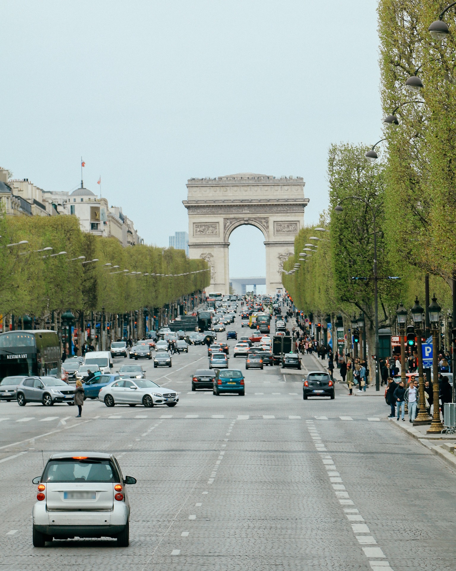 Traffic streams down a tree-lined Parisian avenue toward the Arc de Triomphe