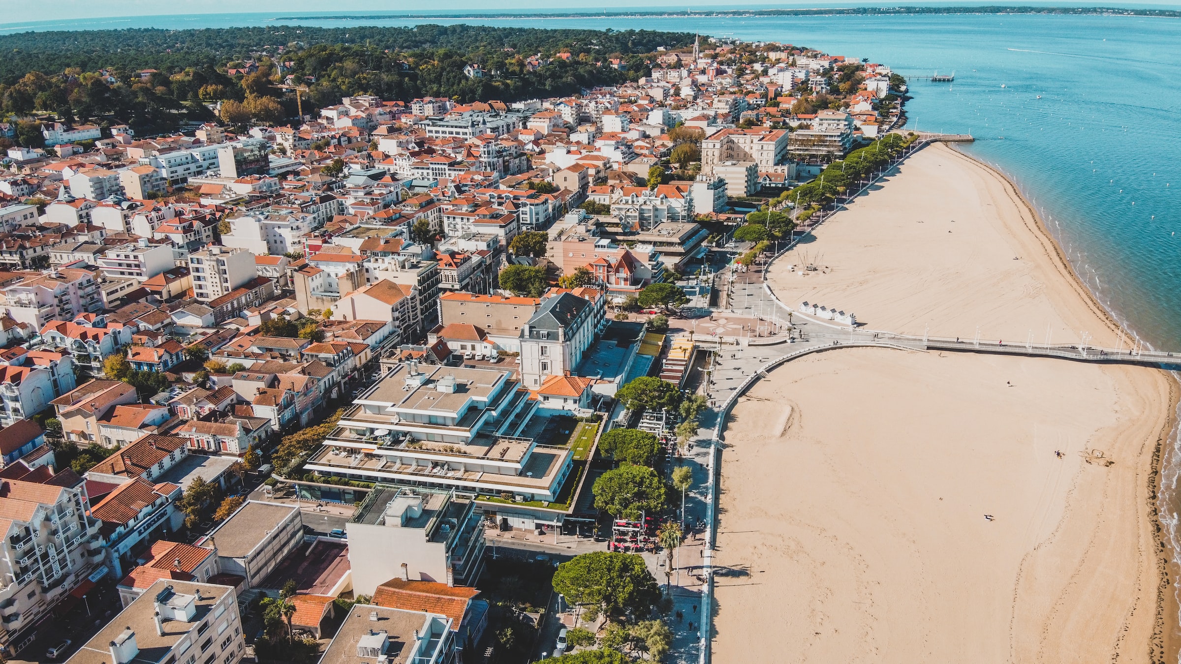Teen travelers look out over a coastal town with a sandy beach curving along the waterfront