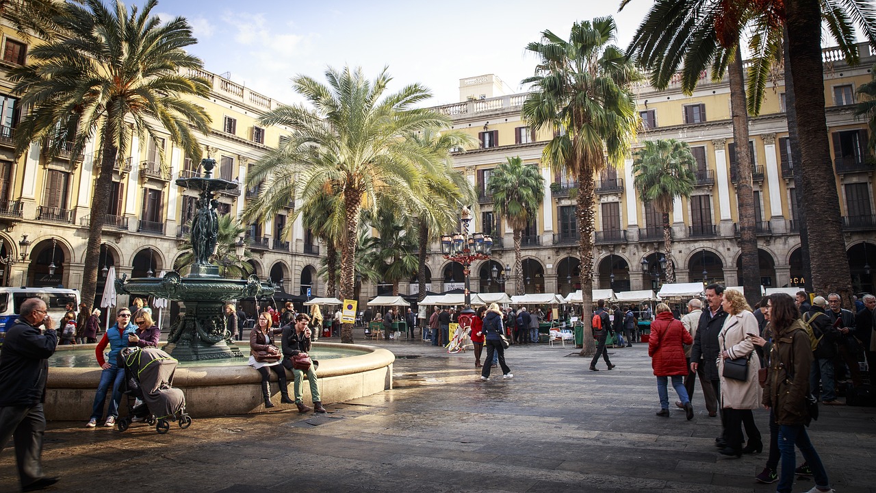 A palm-lined plaza with a fountain surrounded by historic buildings and passersby