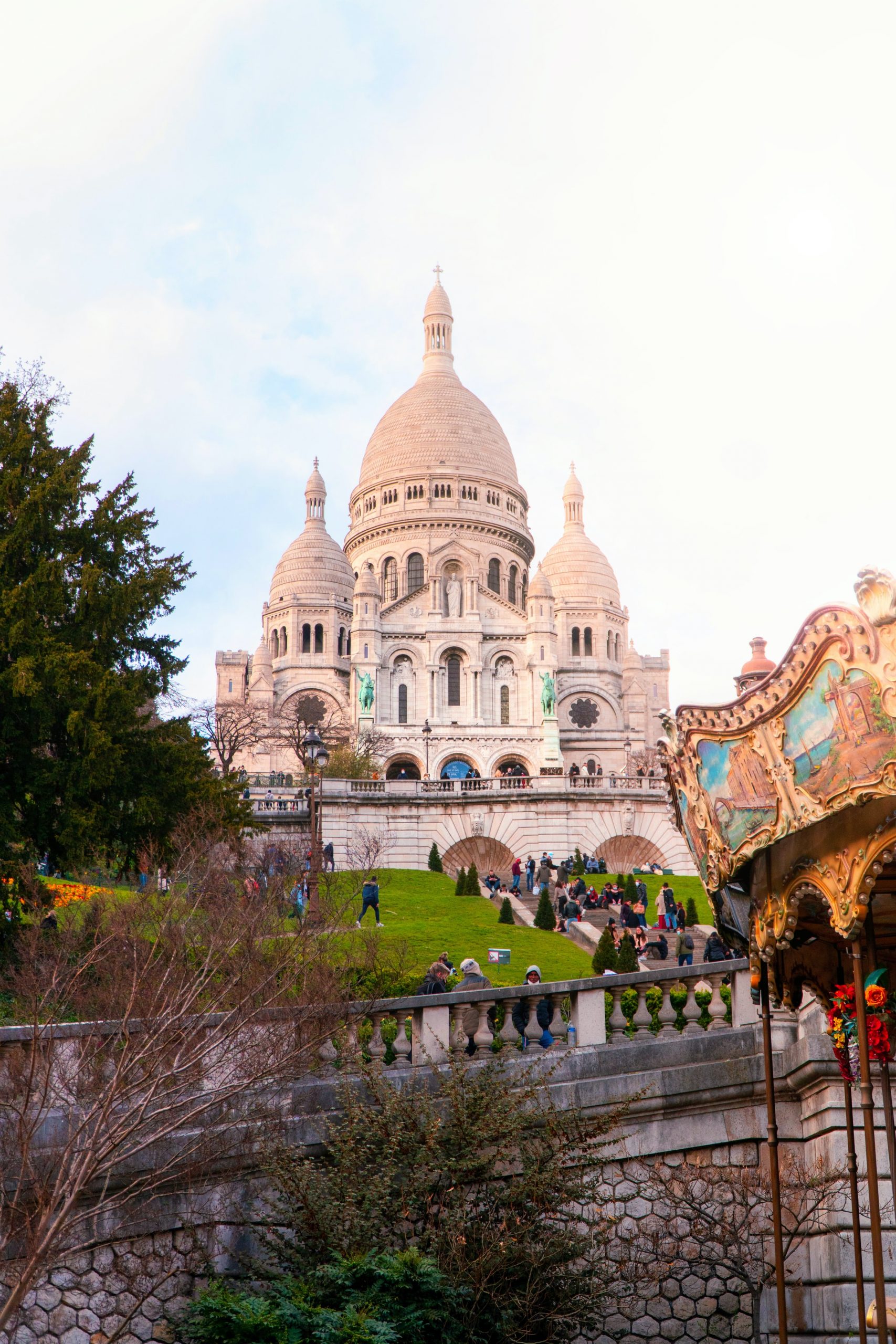 Sacré-Cœur Basilica rises above Montmartre's gardens, with a carousel roof in the foreground