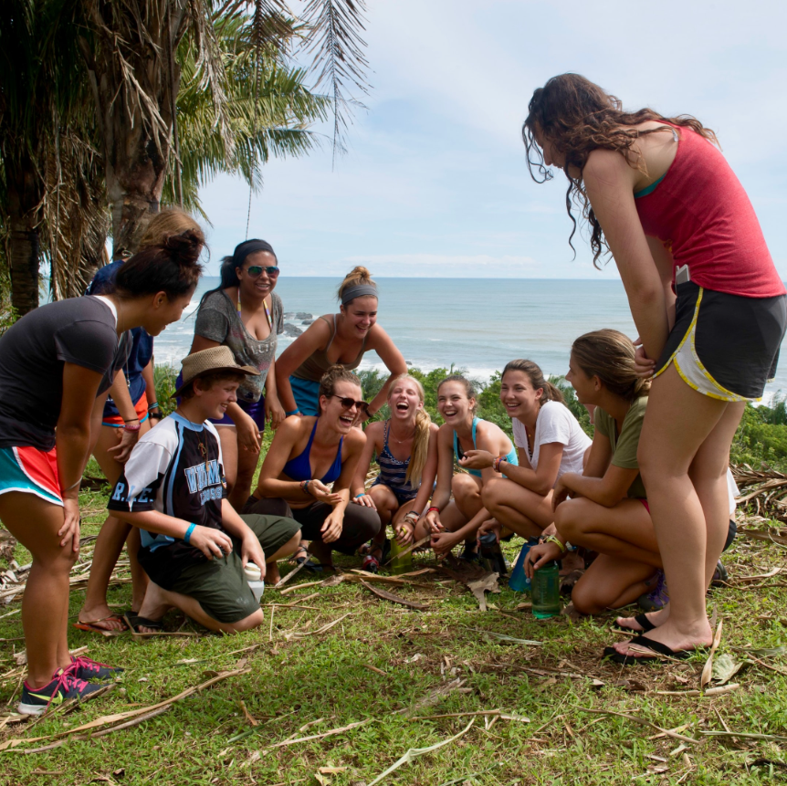 teenagers on their best service trips for teens sitting in a half circle laughing on the grass by the sea
