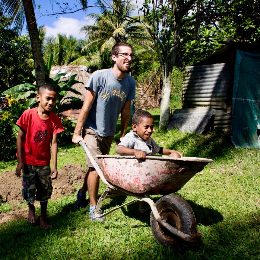 rustic pathways student carrying a local kid in Fiji in a wheelboard and another kid walking beside them while on the best service trips for teens